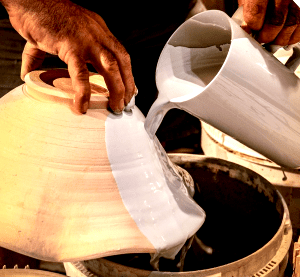 A person pouring liquid glaze onto a pottery piece during the ceramic glazing process.