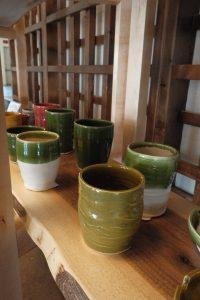 Several green and white ceramic cups with wood-colored rims displayed on a wooden shelf.
