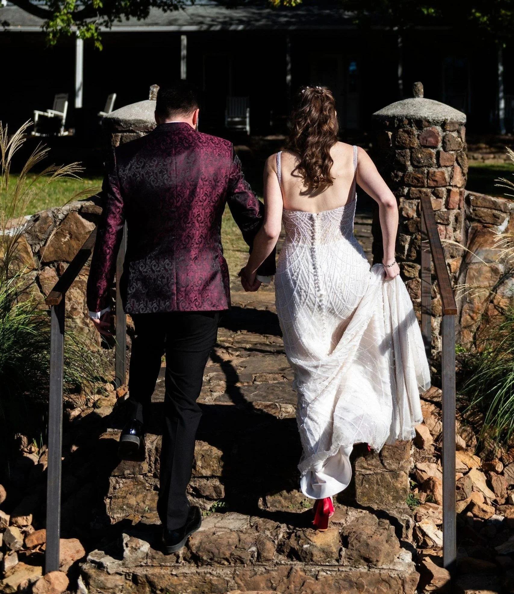 A couple holding hands walking down a stone path at sunset with stone columns on each side.