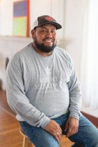 Man in a baseball cap and gray shirt sitting and smiling