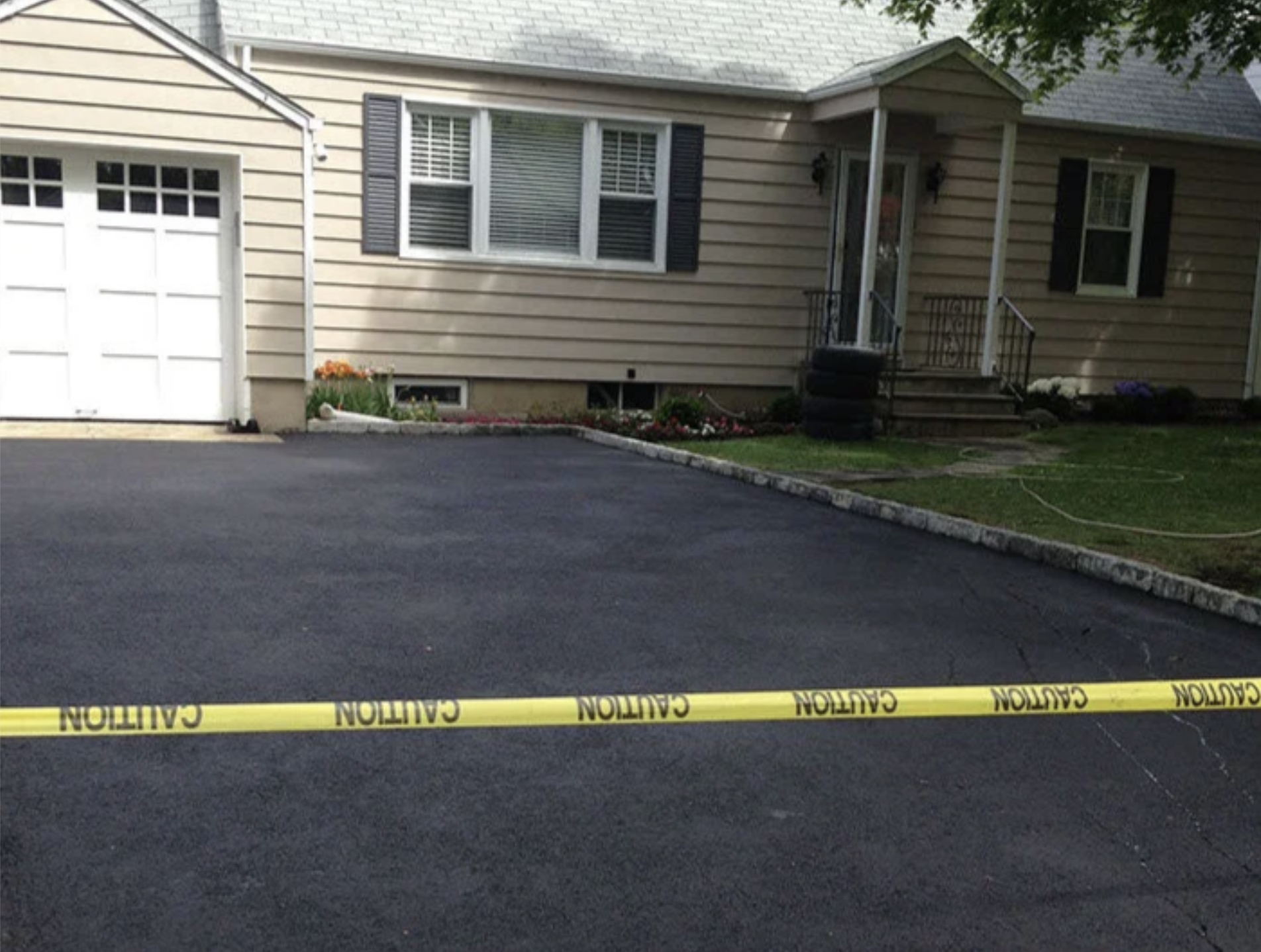 A residential house with a driveway, flower bed, and caution tape across the front yard.