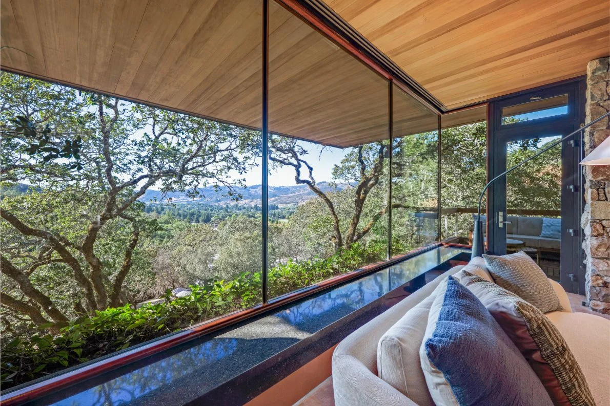 Living room with large glass windows showing trees and a scenic landscape outside.