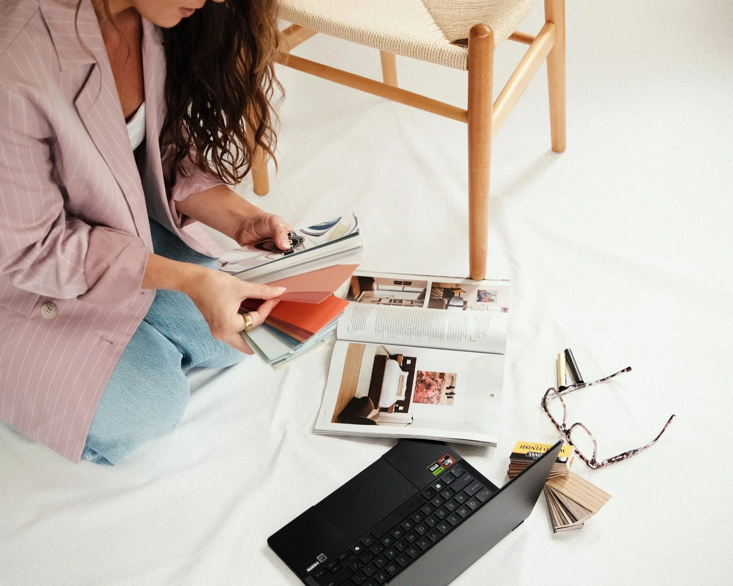 Interior designer reviewing paint colors, wood stains, and metal finishes alongside a laptop and design magazine during the creative process