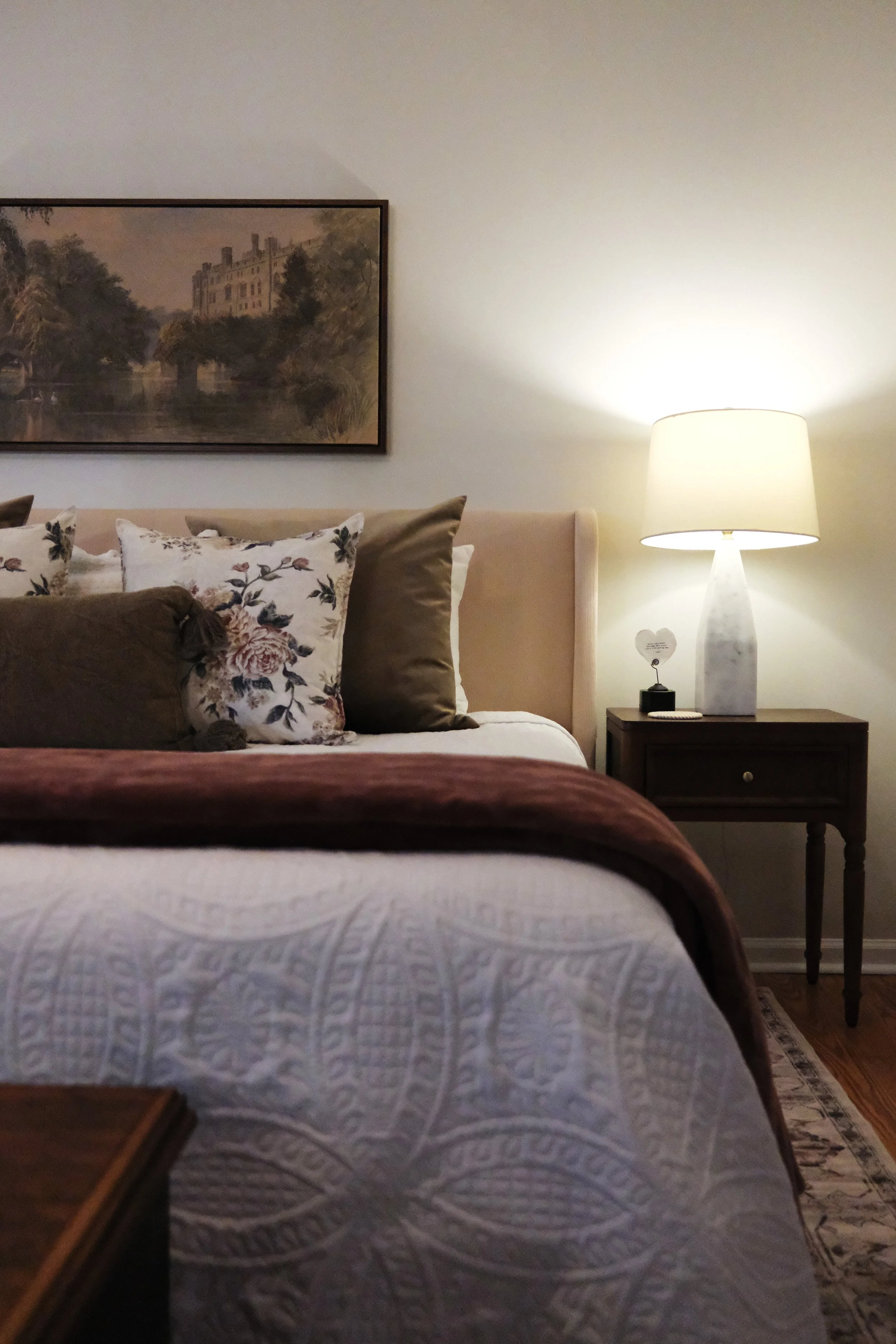 Moody, vintage-inspired Airbnb bedroom with layered floral textiles, collected artwork, a vintage wood nightstand, marble lamp, and patterned rug