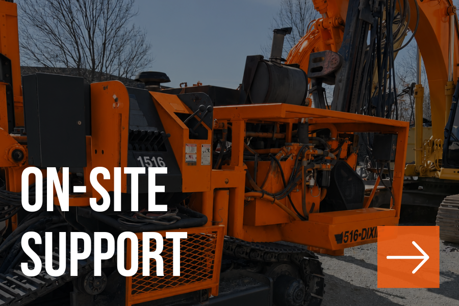 Close-up of an orange piece of heavy construction equipment, possibly a drill or excavation machine, outdoors with trees in the background.