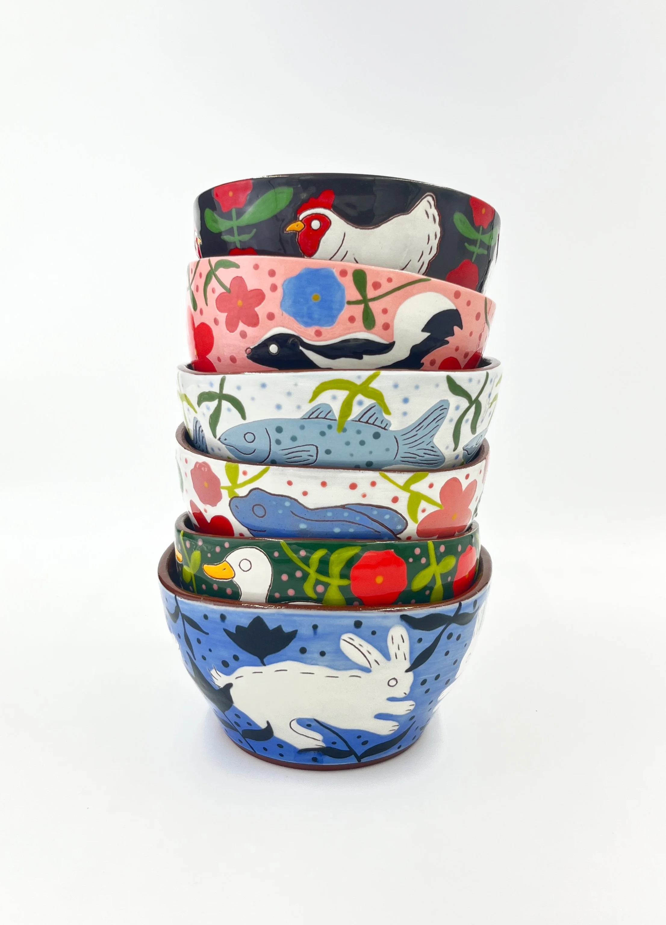 Stacked ceramic bowls with colorful animal and floral designs, topped by a black bowl with chickens and red flowers, set against a white background.