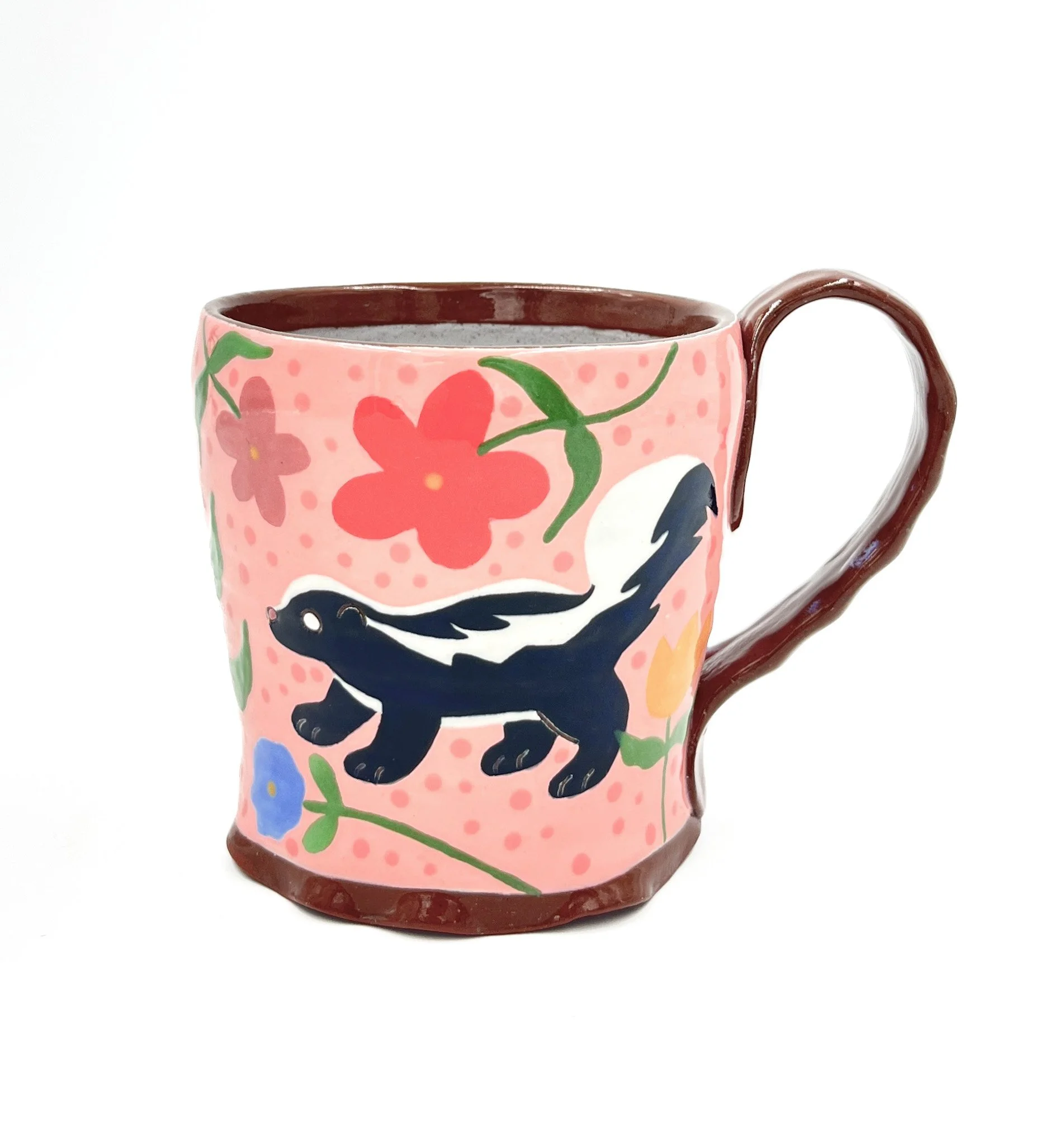 Hand-painted ceramic mug with pink background, decorated with colorful flowers, a blue whale with a white belly, and green leaves, against a white background.