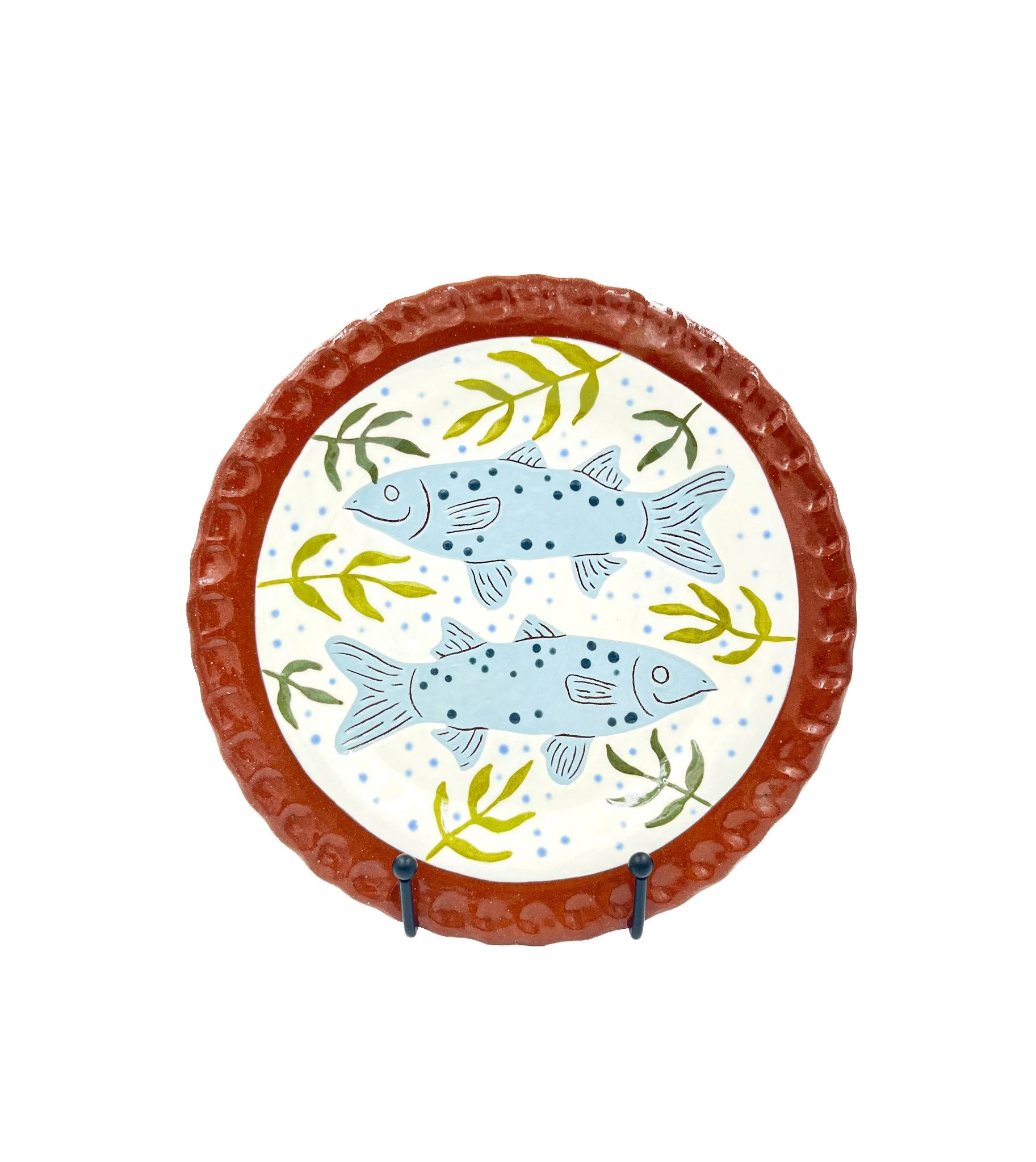 Decorative dish with painted fish and plant design, surrounded by a red textured outer rim, displayed on a stand.