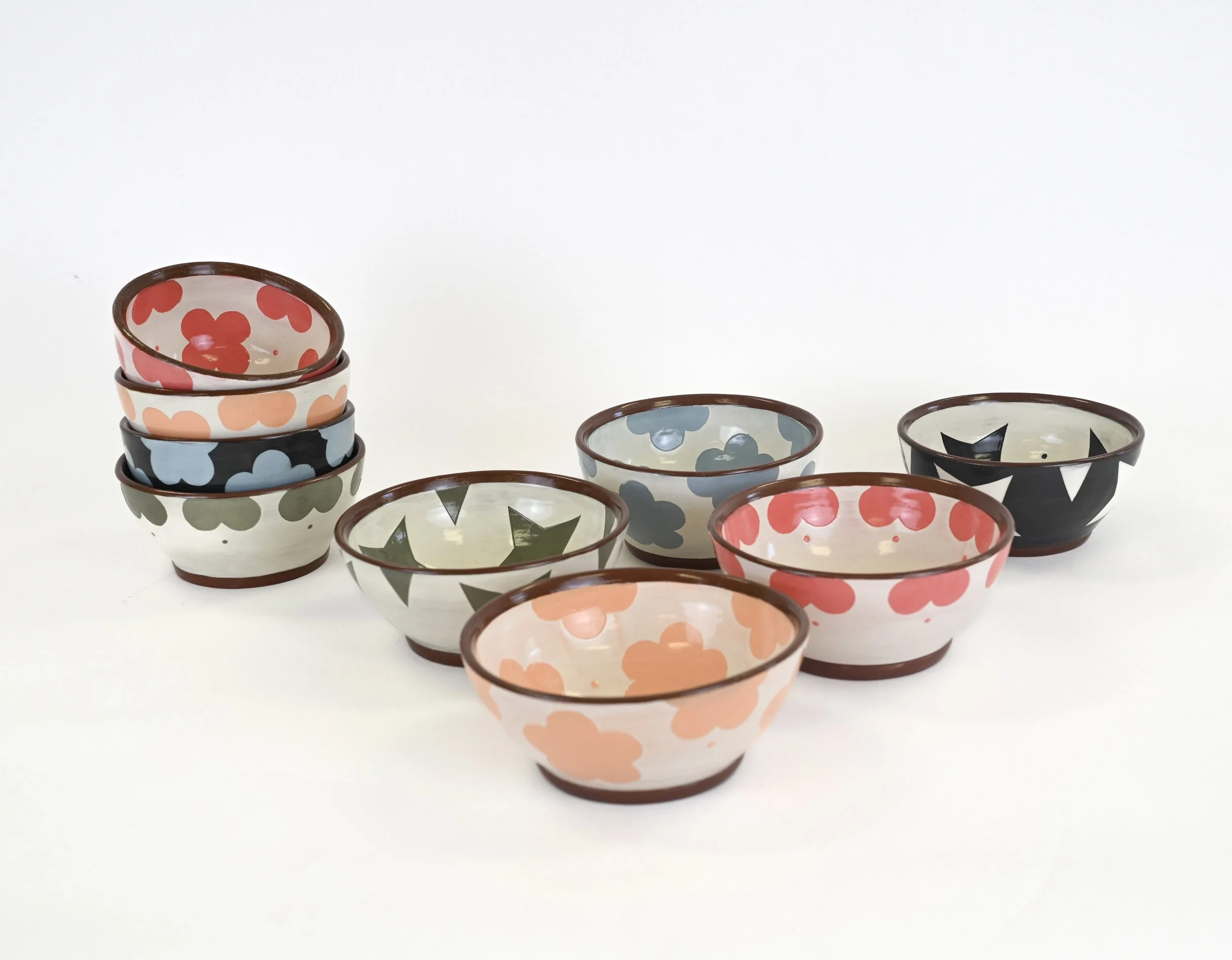 Stacked small bowls with various colorful patterns, including hearts, stars, and flower designs, on a white background.