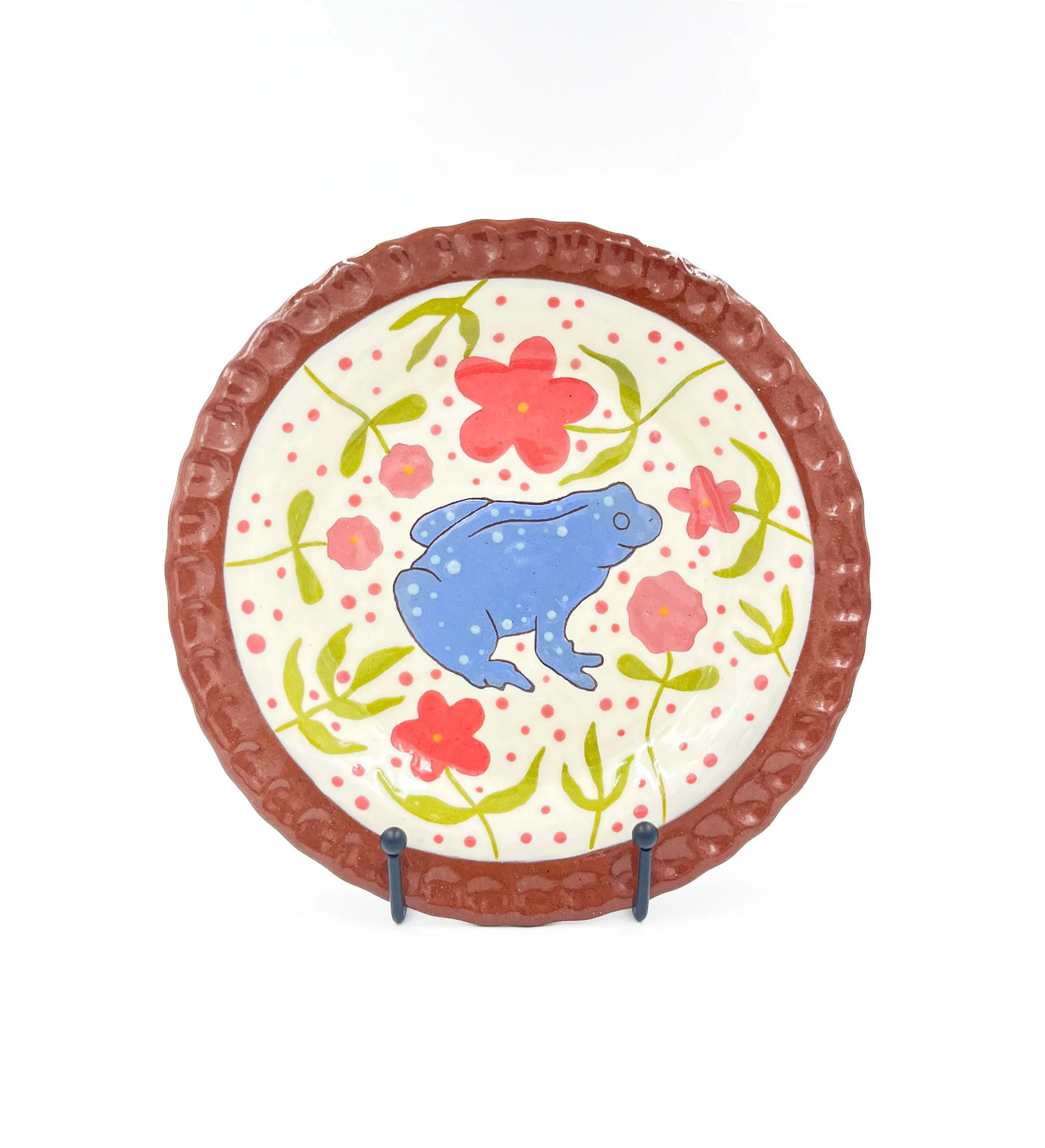 Decorative hand-painted ceramic plate with floral design and a dark border, displayed on a black stand against a white background.