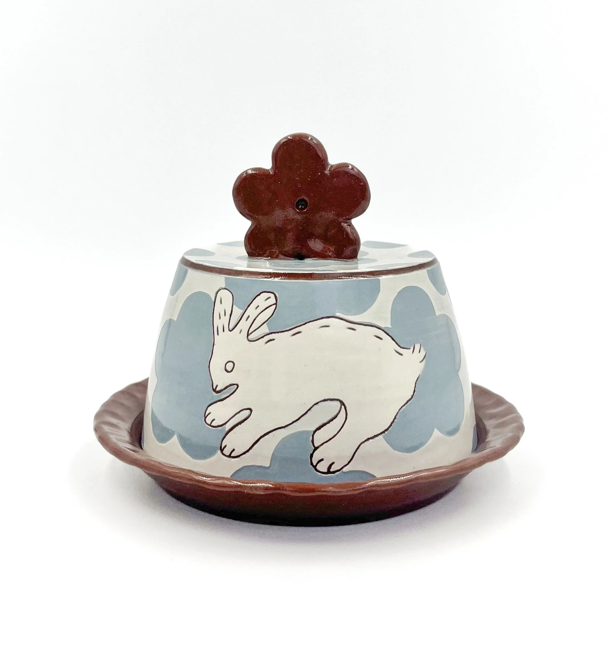 A ceramic figurine of a rabbit on top of a decorated cup. The figurine is white with black outlining, the cup features a pattern of polka dots and a rabbit illustration.