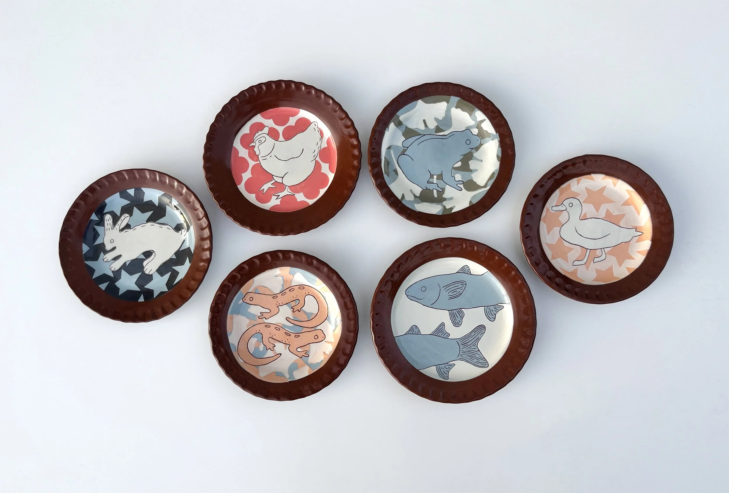 Collection of decorative plates with animal illustrations, including a chicken, frog, rabbit, duck, and fish, arranged on a white background.