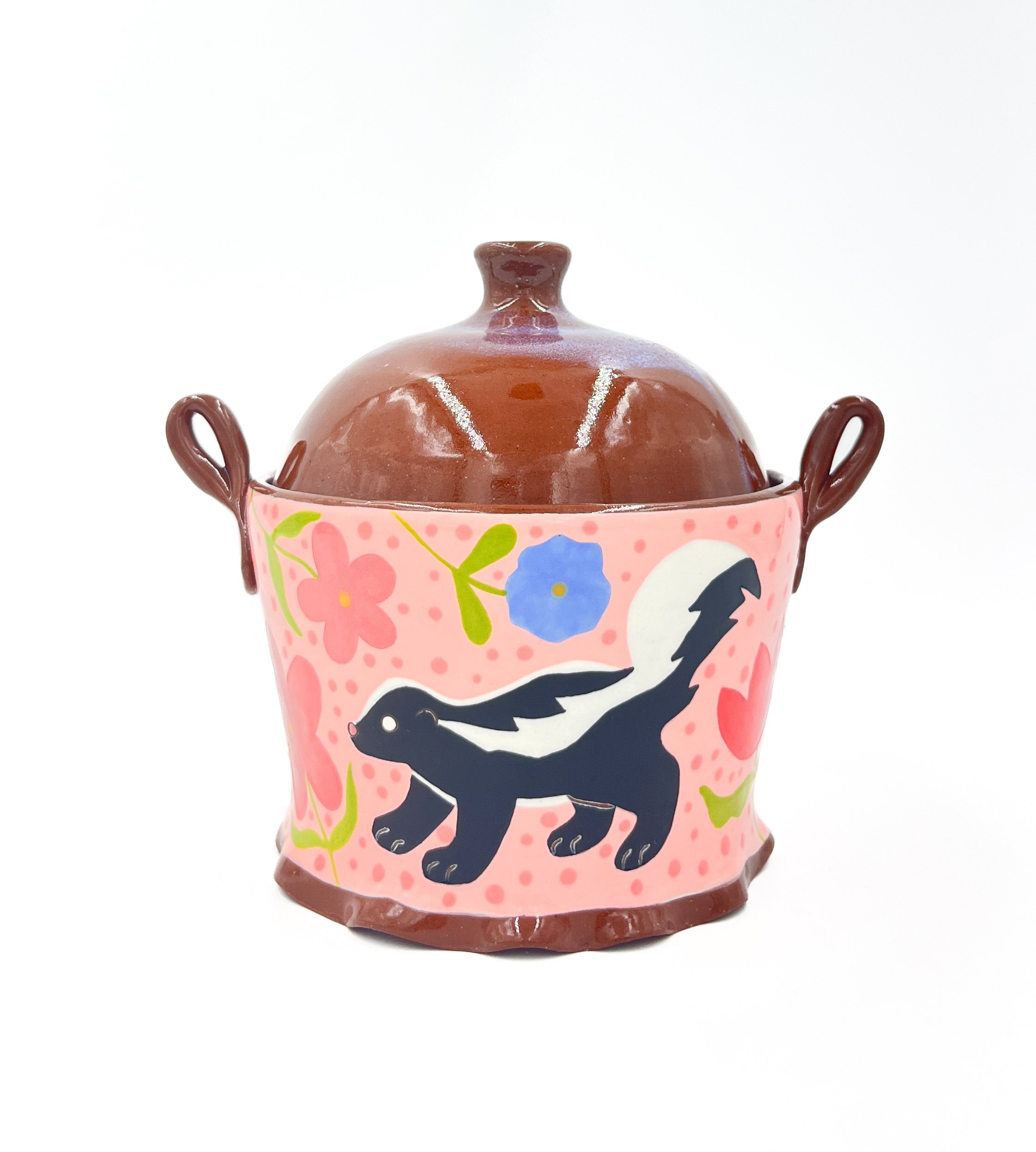 A decorative ceramic container with a domed lid featuring a small rounded knob. The container's body is pink with floral and bird illustrations, including a dark bird silhouette, and has dark brown handles on each side. The background is plain white.