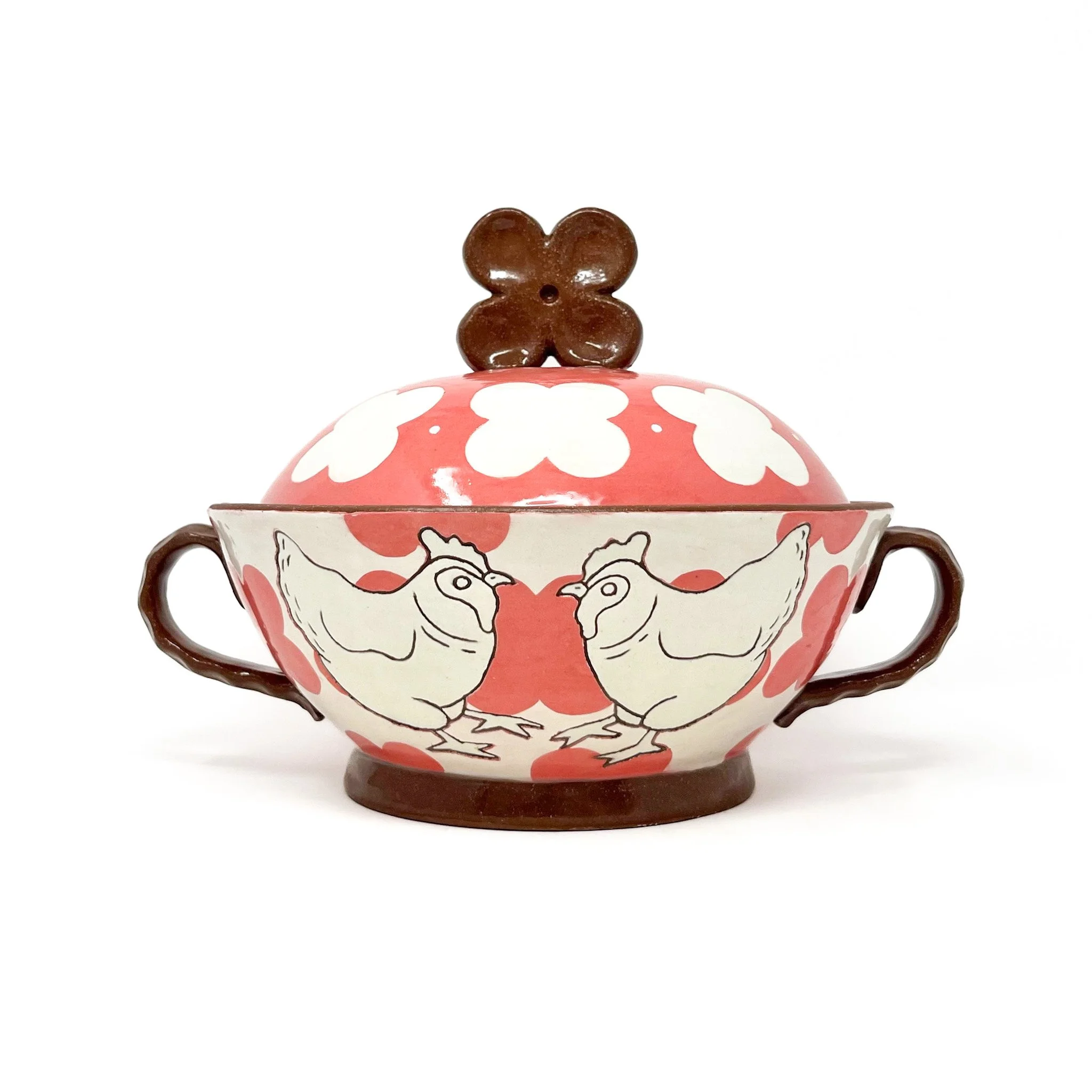A decorative bowl with a pink and white pattern, featuring a seated chicken figure and a small dark brown bear-shaped object on top.