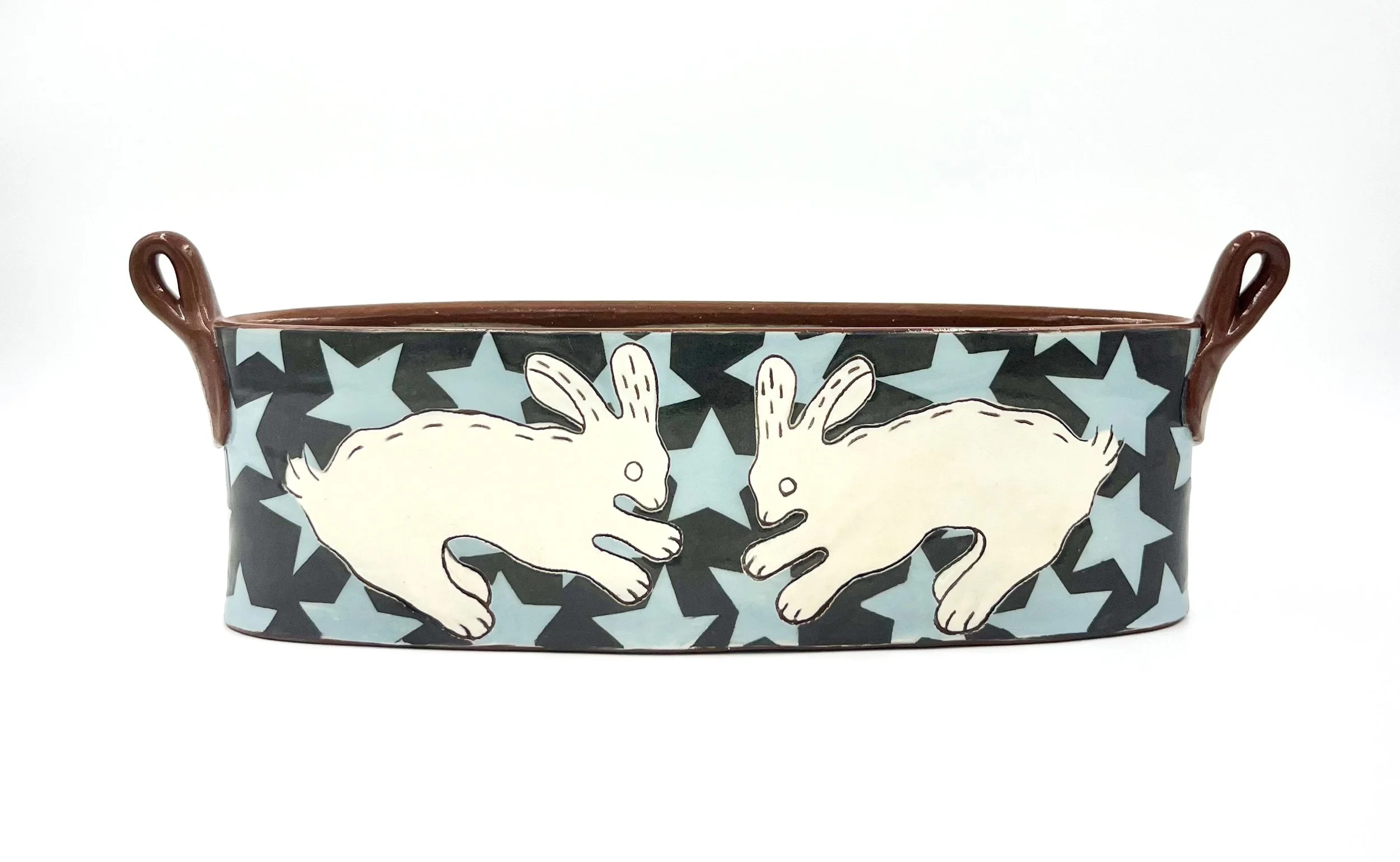 Decorative ceramic bowl with two brown handles and a design featuring white rabbits and blue stars.