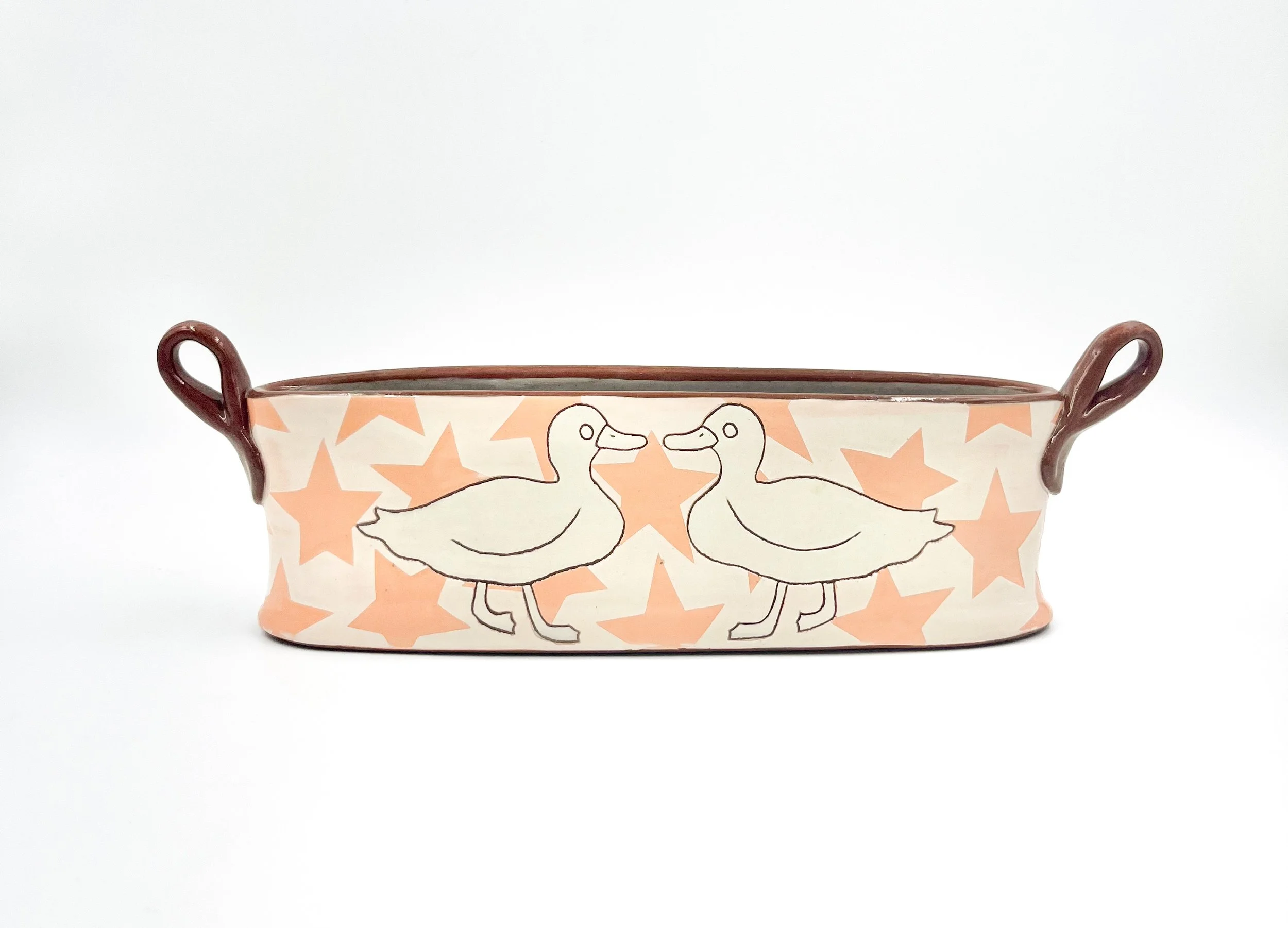 A ceramic bowl with two handles featuring a design of two white ducks facing each other, surrounded by a pattern of pink stars on a light background.