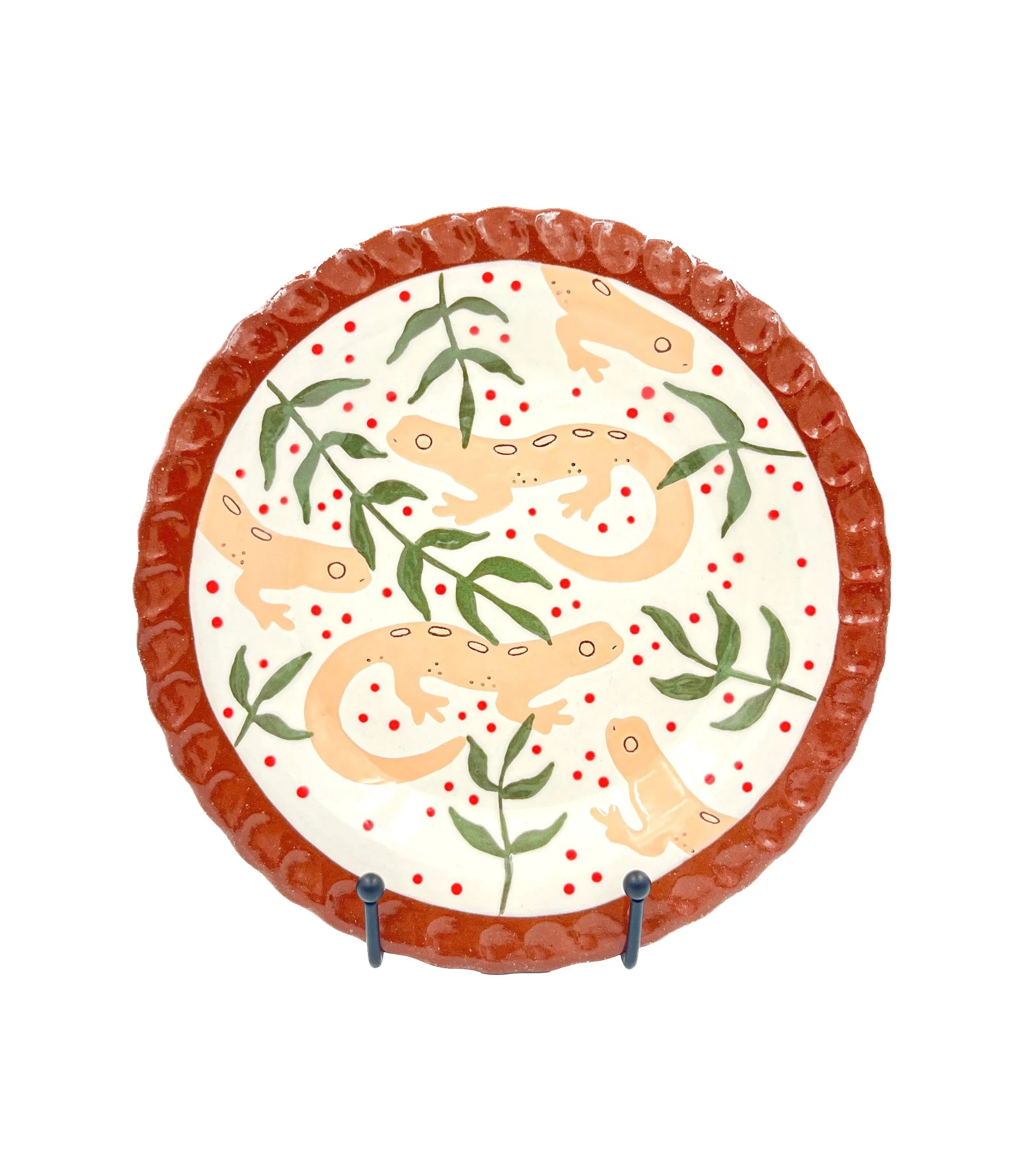 Decorative plate with a design of orange salamanders and green leaves, surrounded by a red ruffled border, on a white background, displayed on a metal stand.