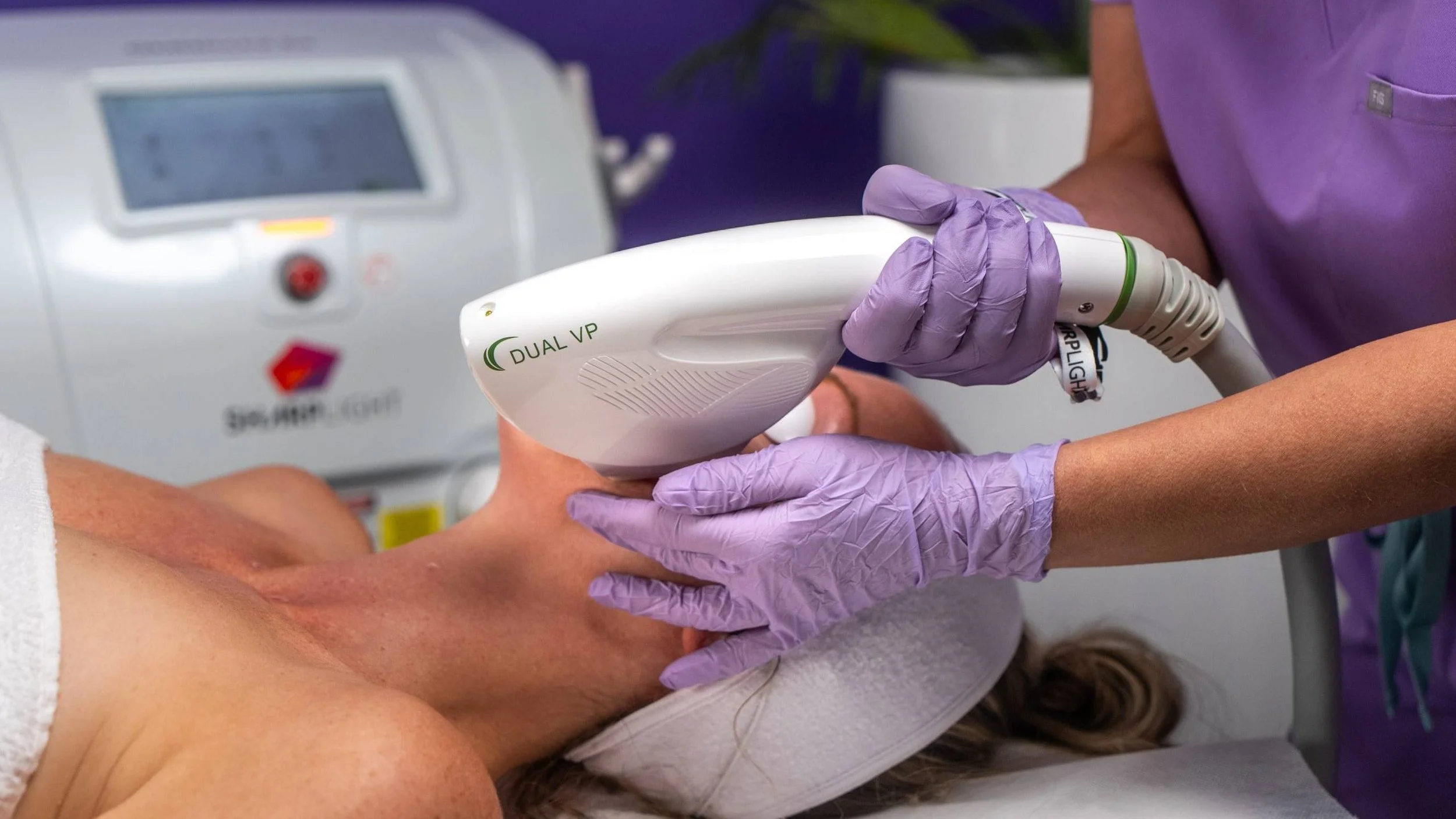 A healthcare professional wearing purple gloves is using a device labeled 'Dual VP' on a patient's forearm during a medical procedure.