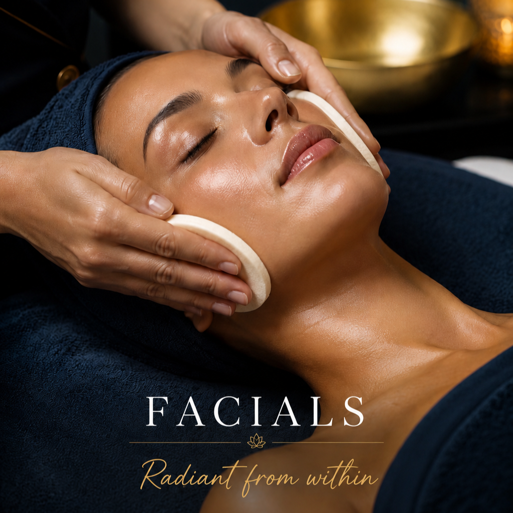 A woman receiving a facial treatment, lying down with her eyes closed, as a skincare professional gently massages her face with hands and foam pads. The setting looks spa-like with warm tones.