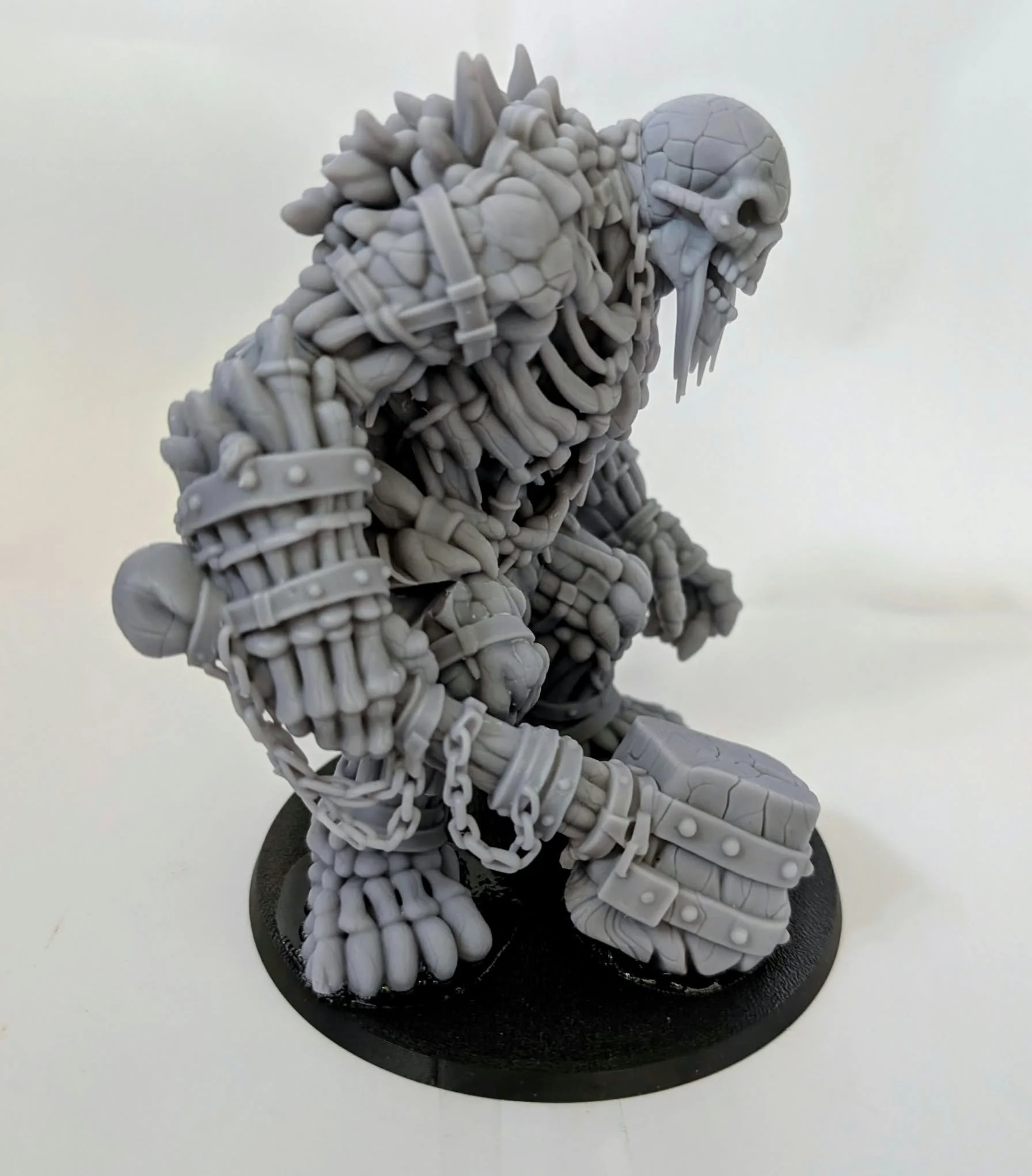 Undead Colossus resin miniature, unpainted, three-quarter view showing its bone plating and chained arms
