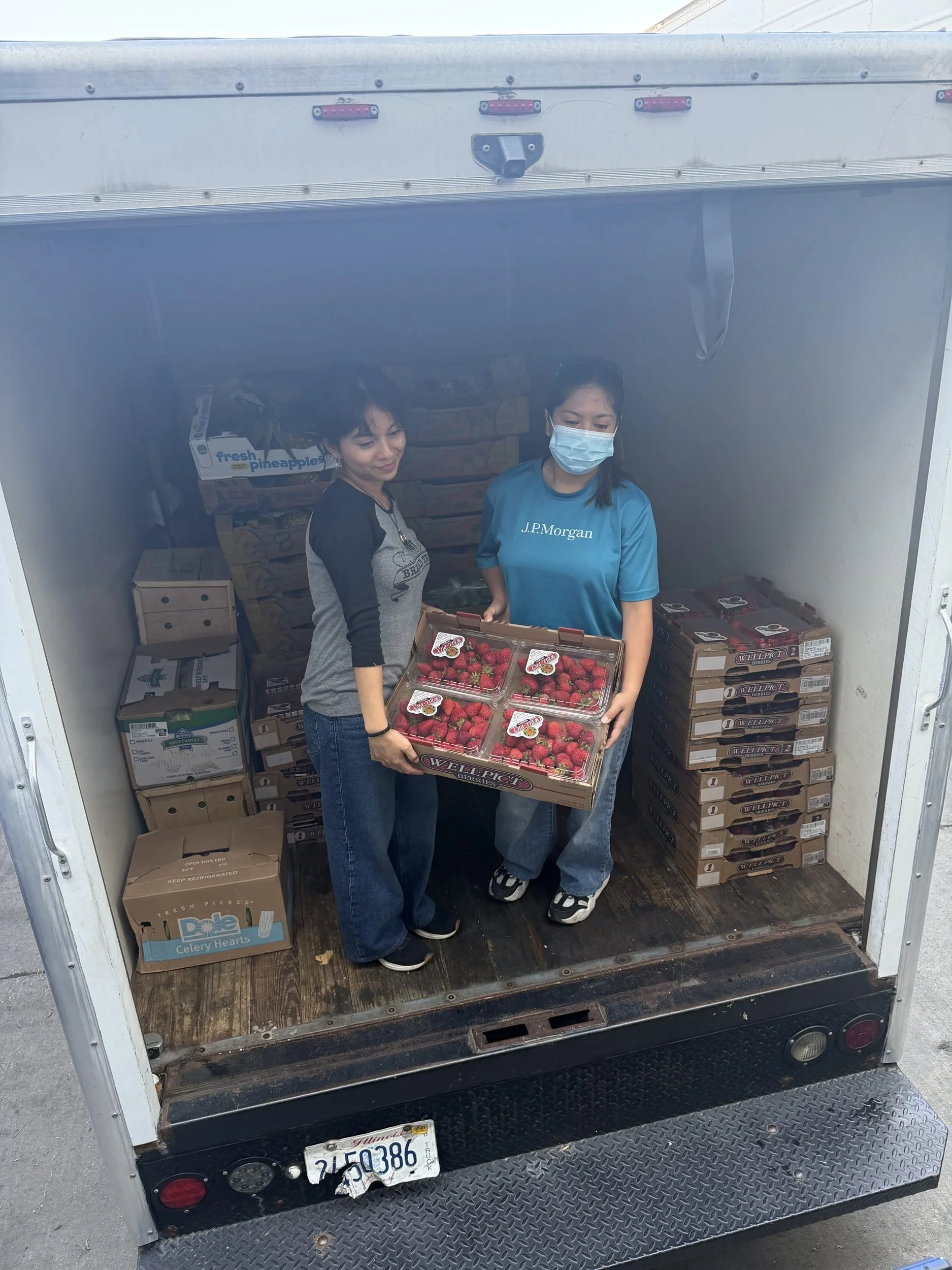 Two volunteers holding a crate of fresh strawberries inside the Port Ministries Bread Truck