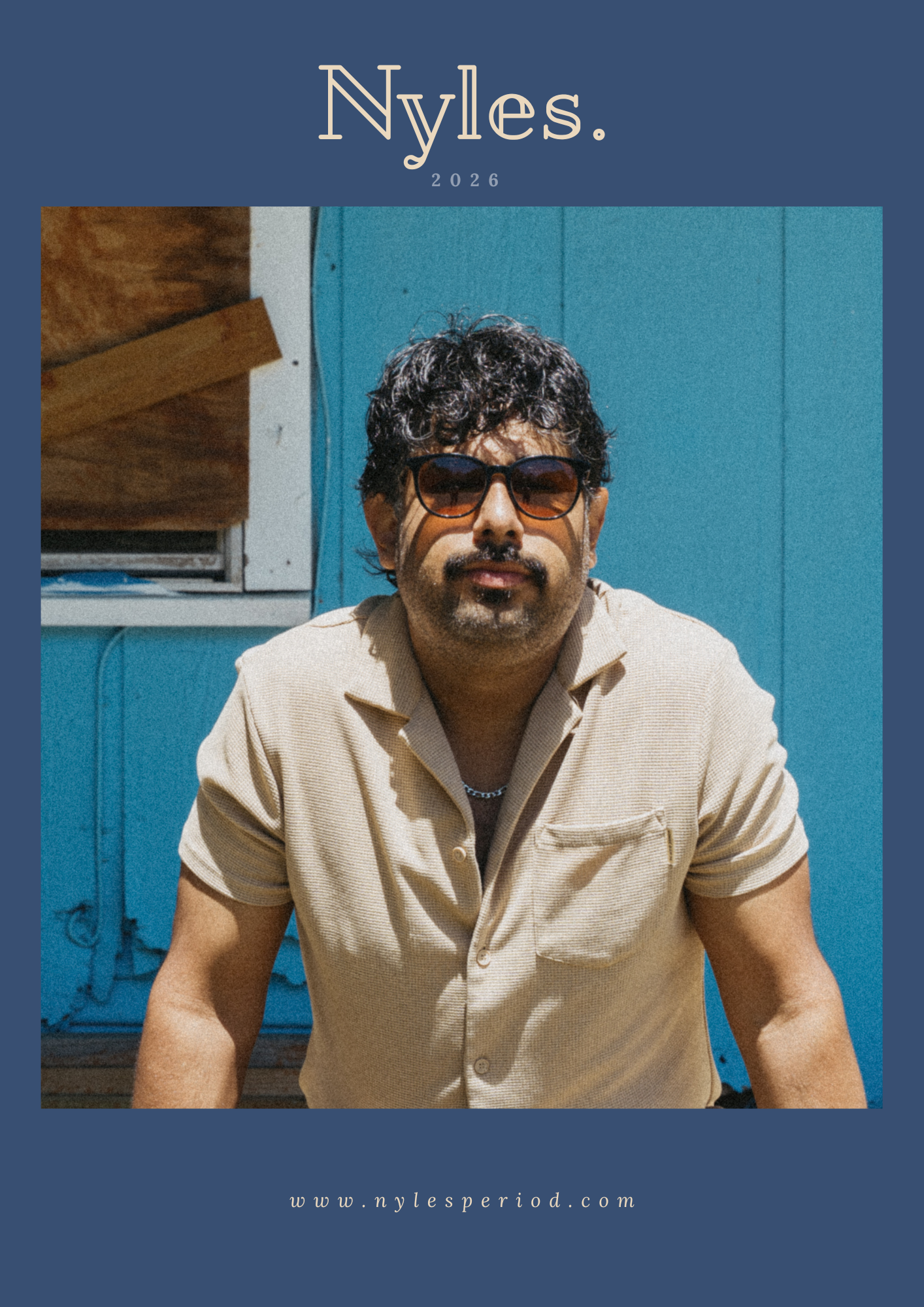 A man with dark curly hair, sunglasses, and a beige short-sleeve shirt is sitting outdoors in front of a blue wall. The photo has a blue border with the text 'Nyles. 2026' at the top and the website 'www.nylesperiod.com' at the bottom.