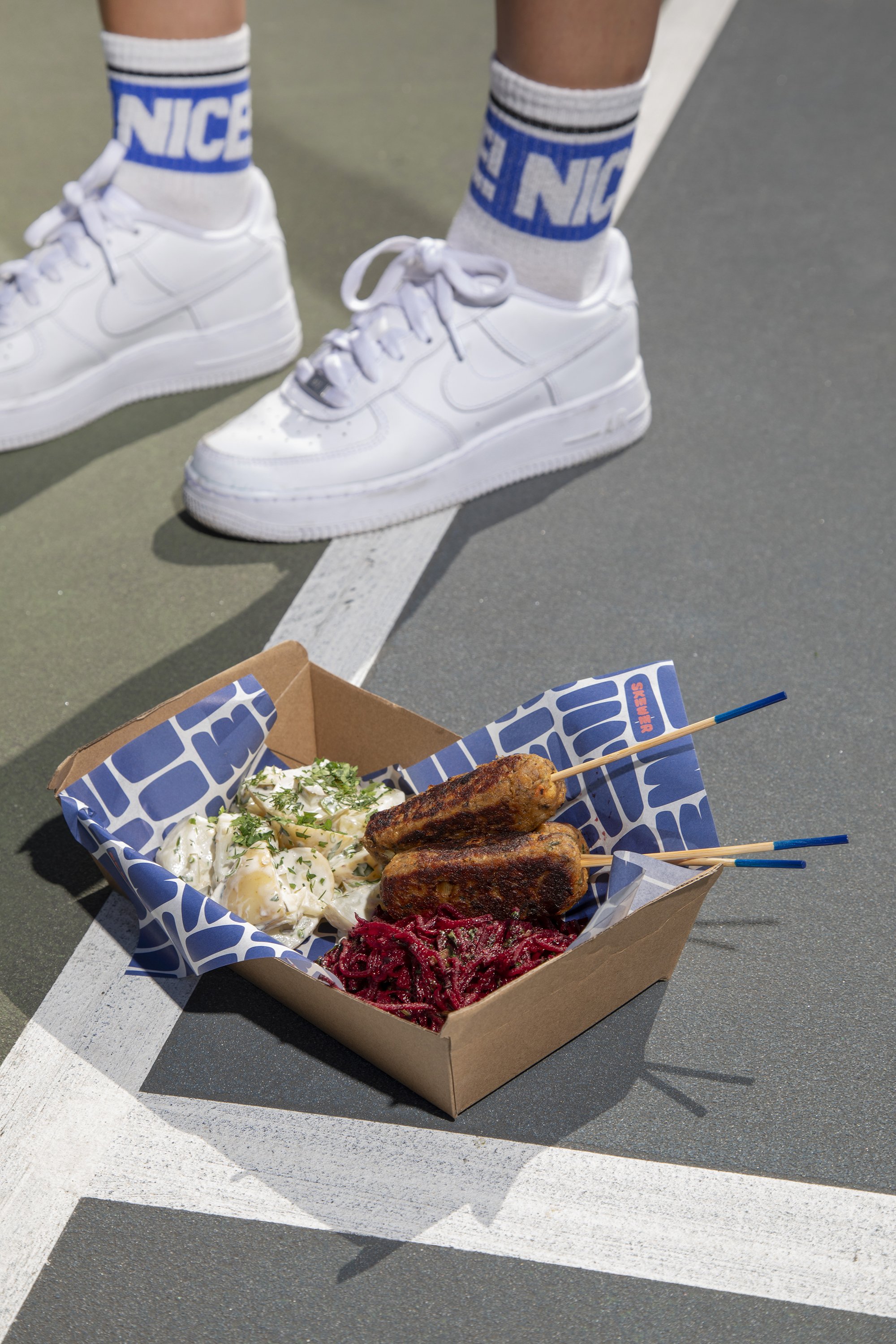 A tray of food with grilled skewers and potato salad on a sports court.
