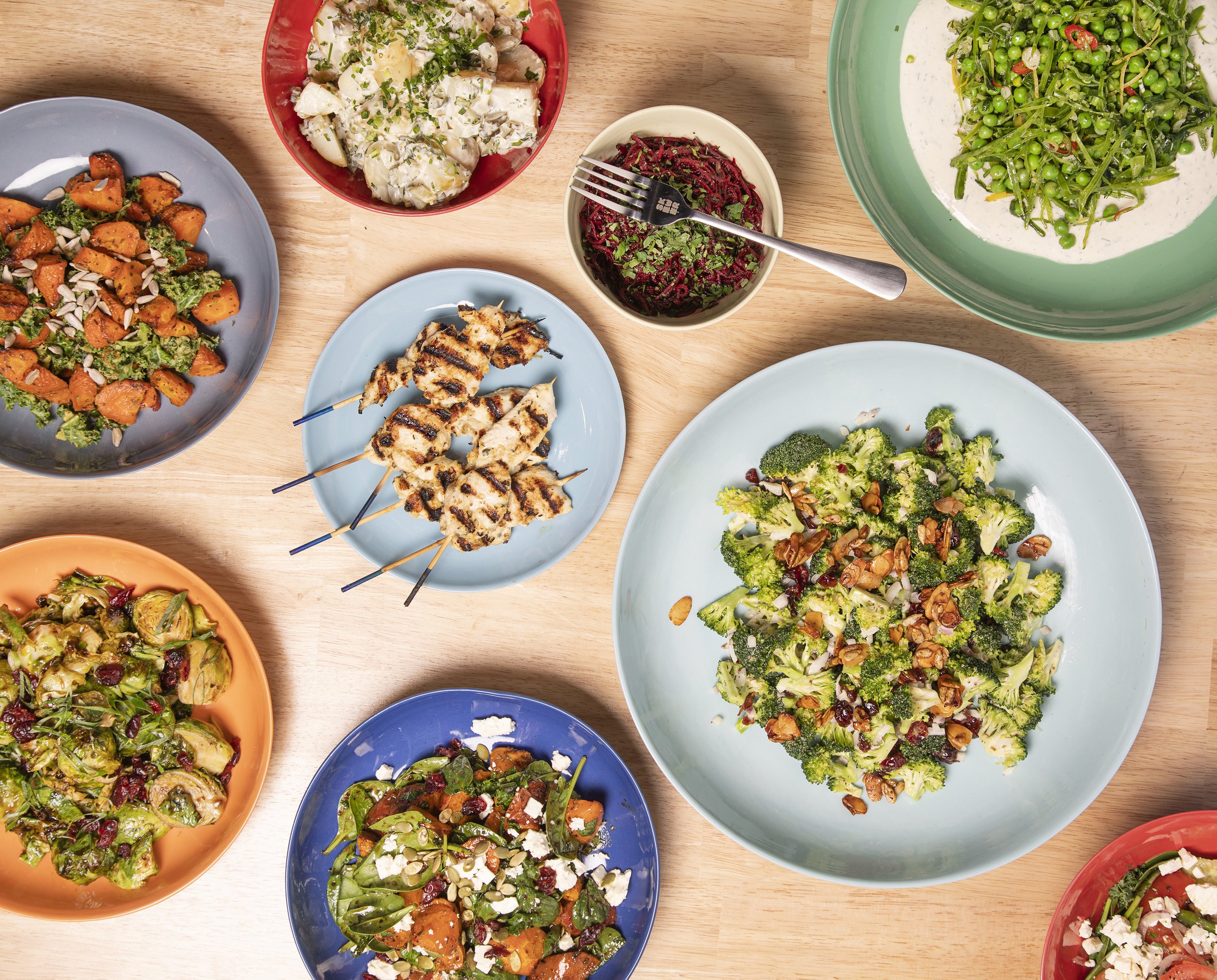 Assorted salads and grilled chicken skewers on a wooden table.