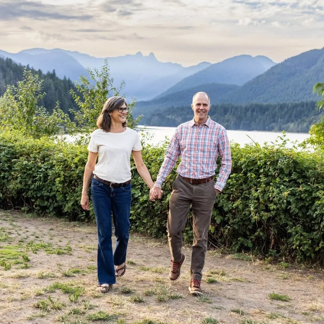 Photo of Shelley Luce and her husband holding hands while walking at Cleveland Dam field, coastal mountains appear in the background.