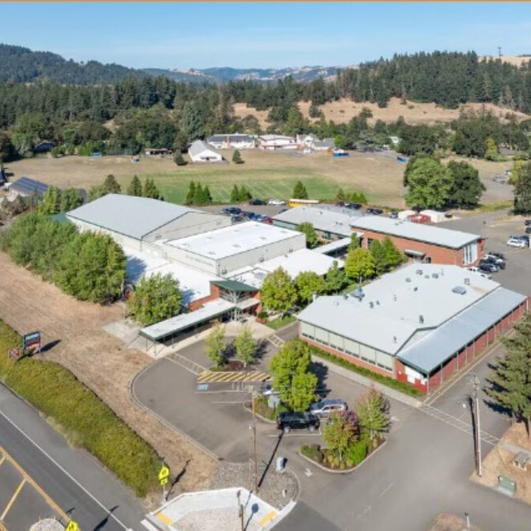 Aerial view of Glide School District Athletic Complex with parking lots, surrounded by trees and hills in the background.