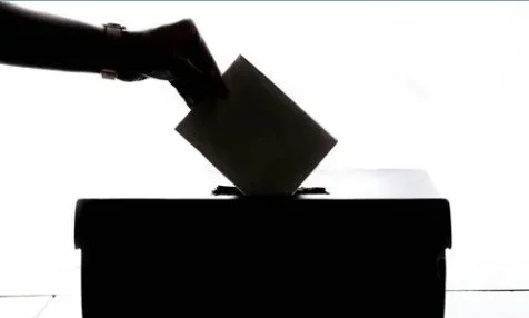 A hand casting a ballot into a ballot box.