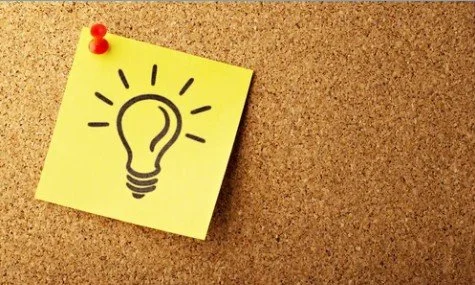A yellow sticky note with a black light bulb drawing is pinned to a corkboard with a red pushpin.