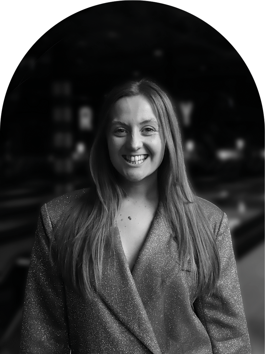 A smiling woman with long hair wearing a sparkly blazer indoors.