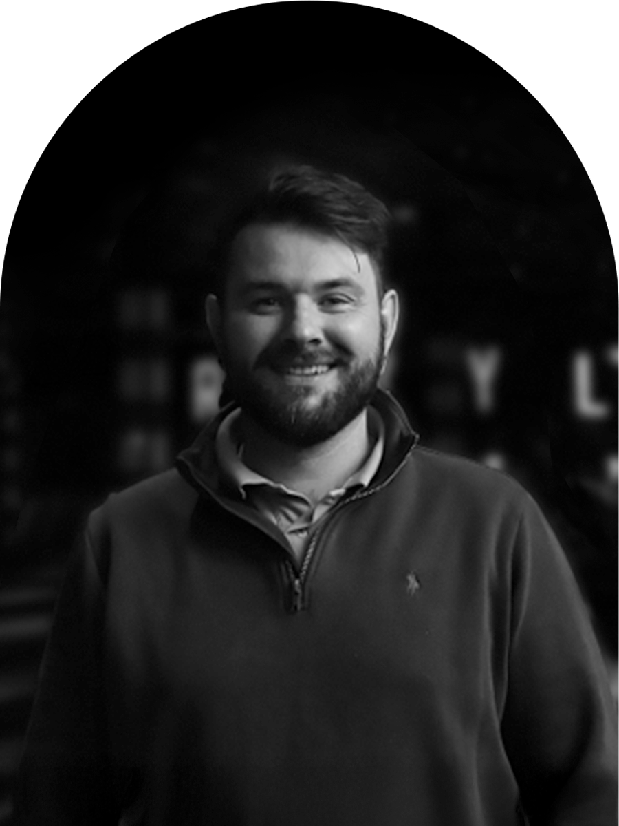 A smiling man with a beard and short hair, wearing a quarter-zip sweater, standing outdoors at night with blurred background.