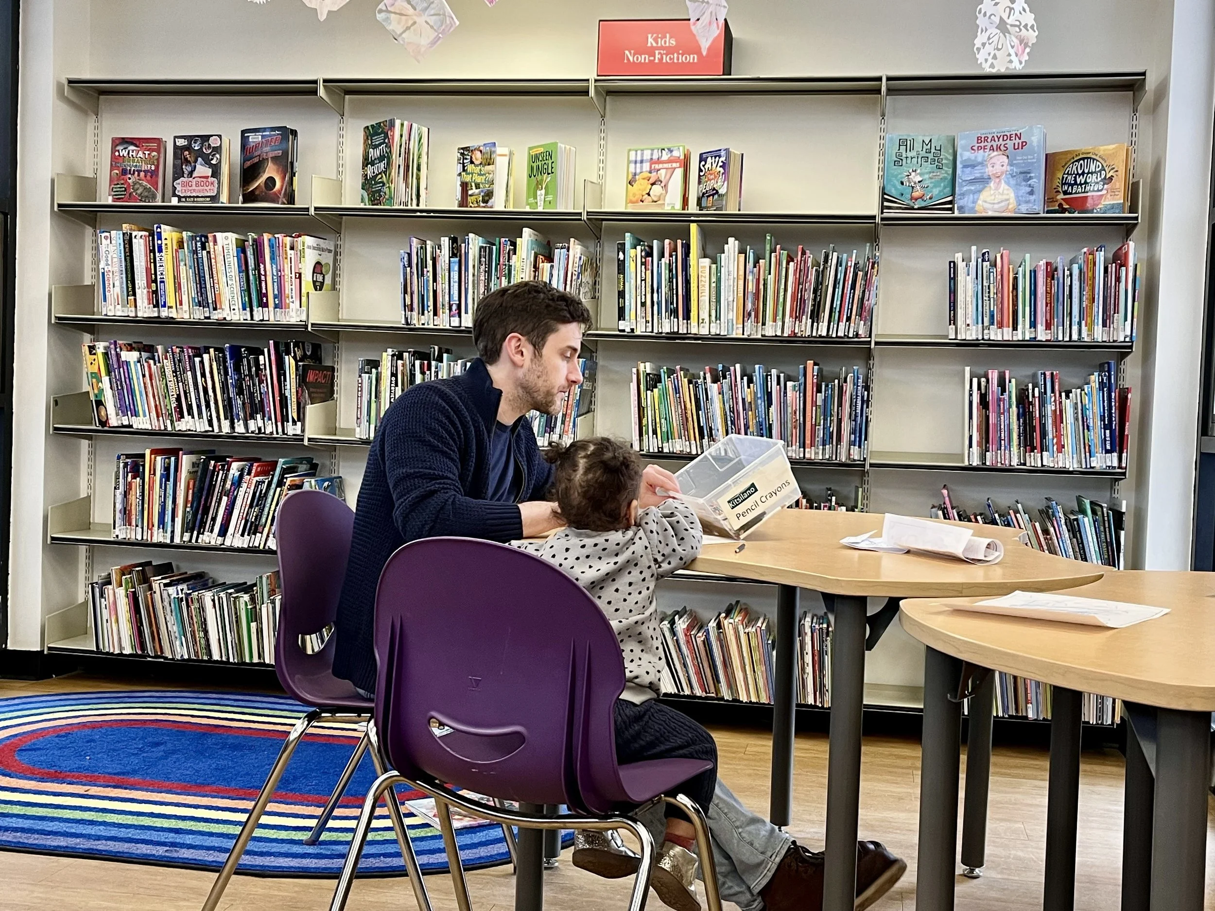 Father and little girl sitting at a table in the library and colouring pictures