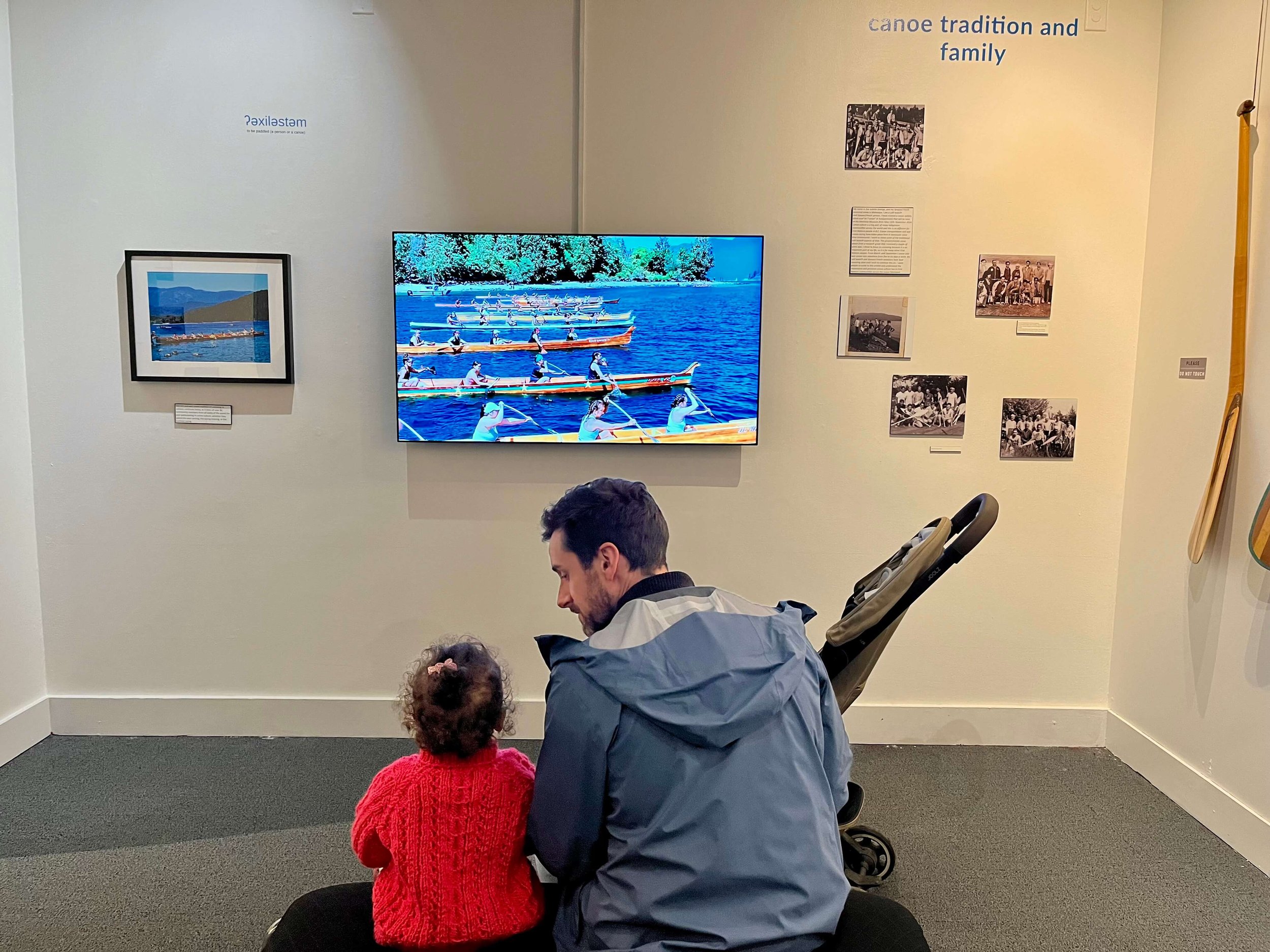 Little girl and her dad looking up at a screen and watching rowers at the Vancouver Maritime Museum