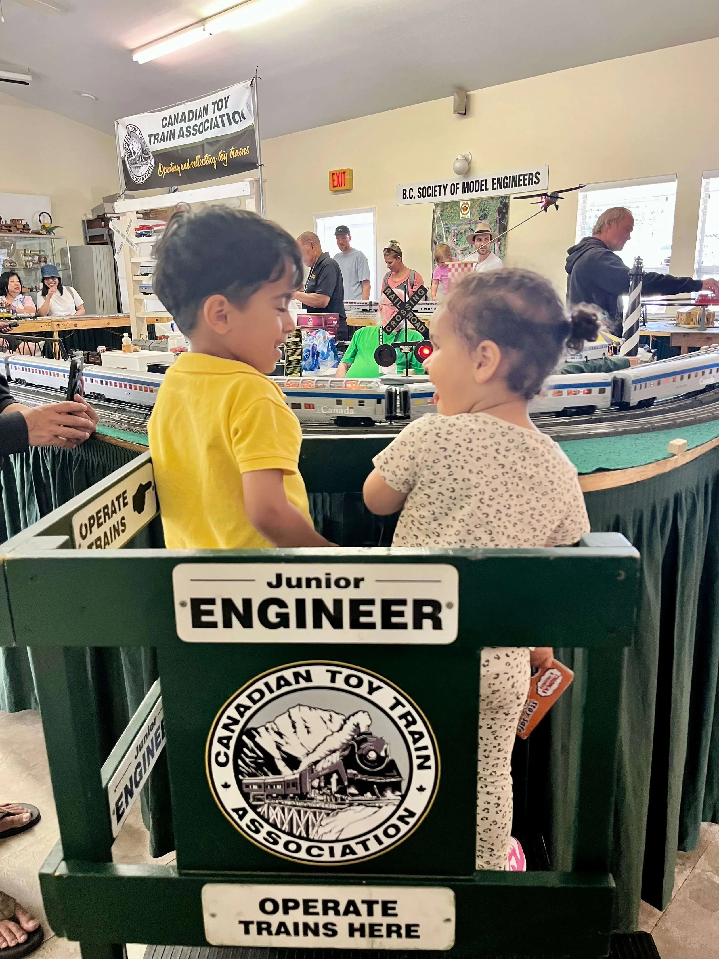 Two young toddlers standing in a seat for Junior Engineers  while watching the mini trains at the Burnaby Central Railway.