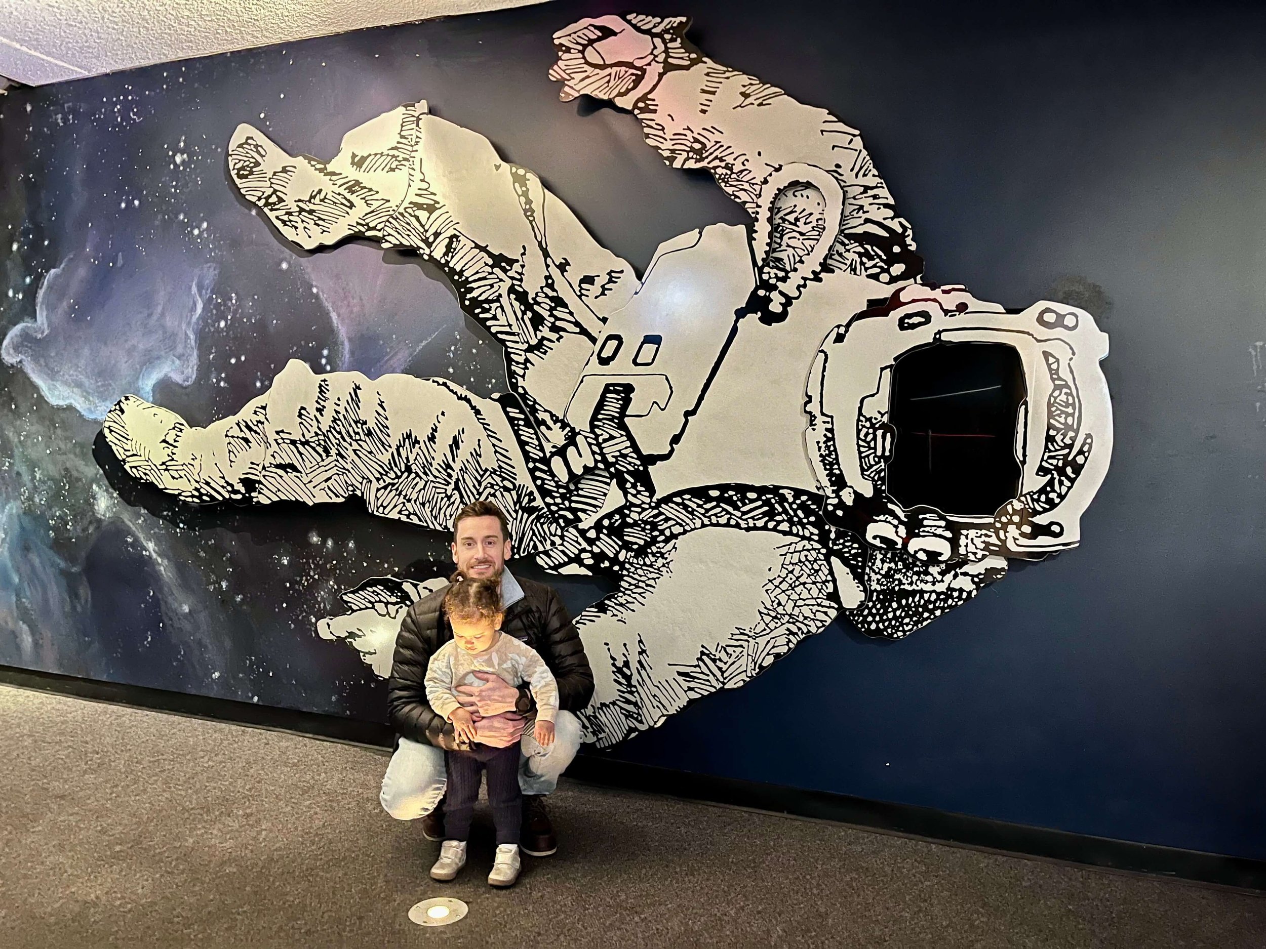 Dad and little girl standing in front of a giant astronaut picture on the wall