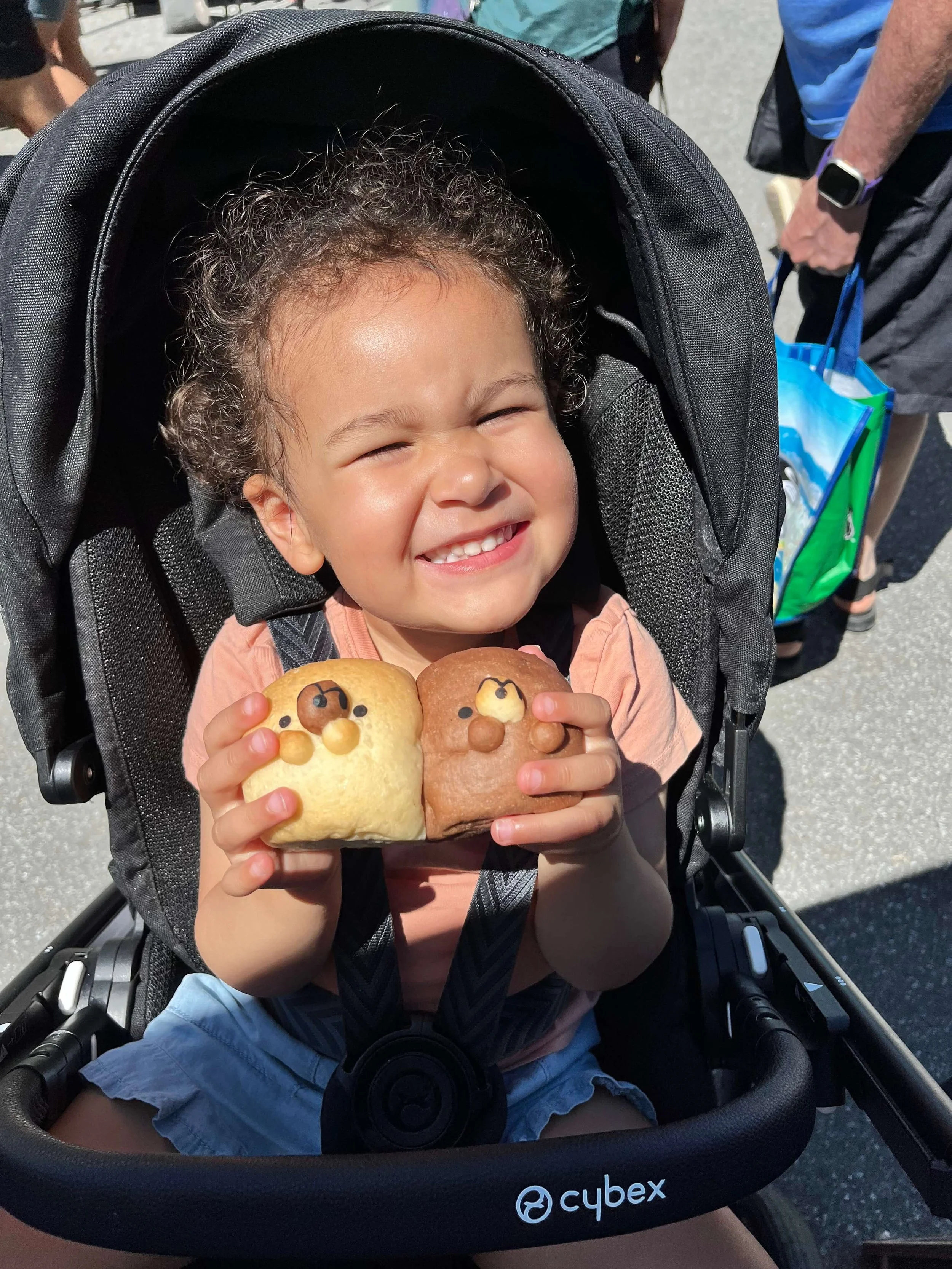 toddler in  stroller. They are smiling and holing up two bread buns with little  bear faces on them