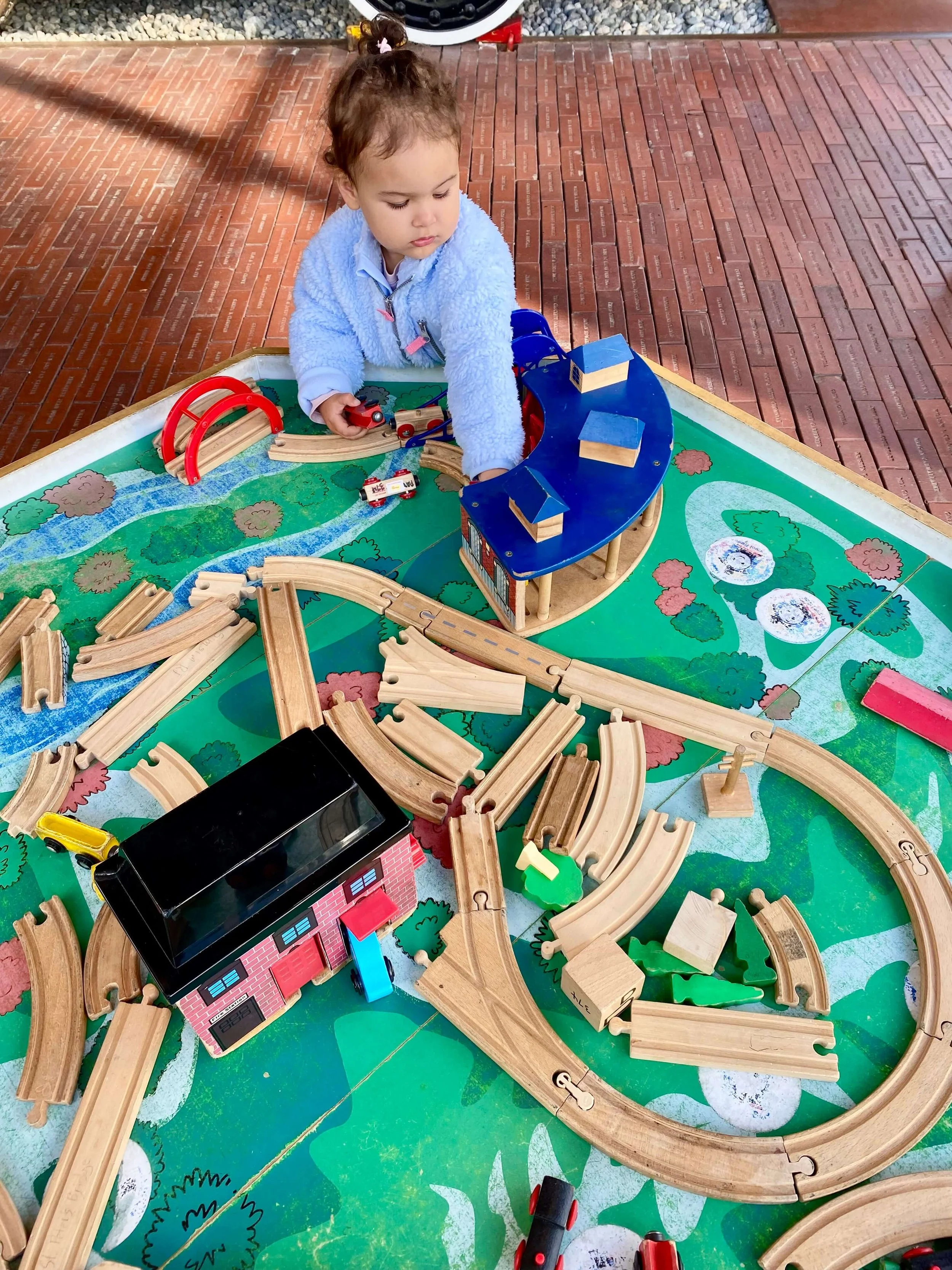 Little girl playing with a wooden train set.