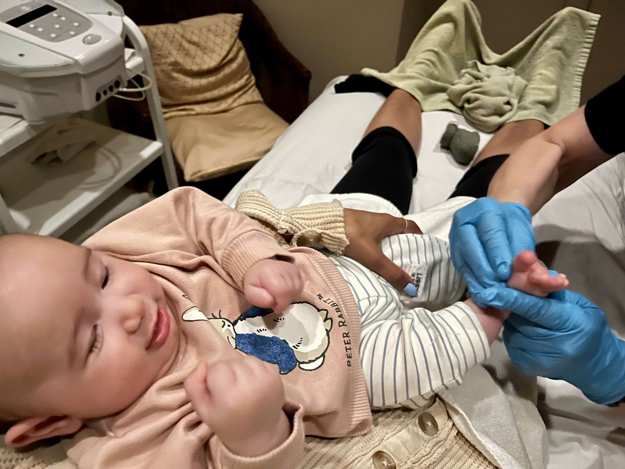 Baby boy lying on his mothers lap while getting reflexology on his baby feet at Le Petit Spa