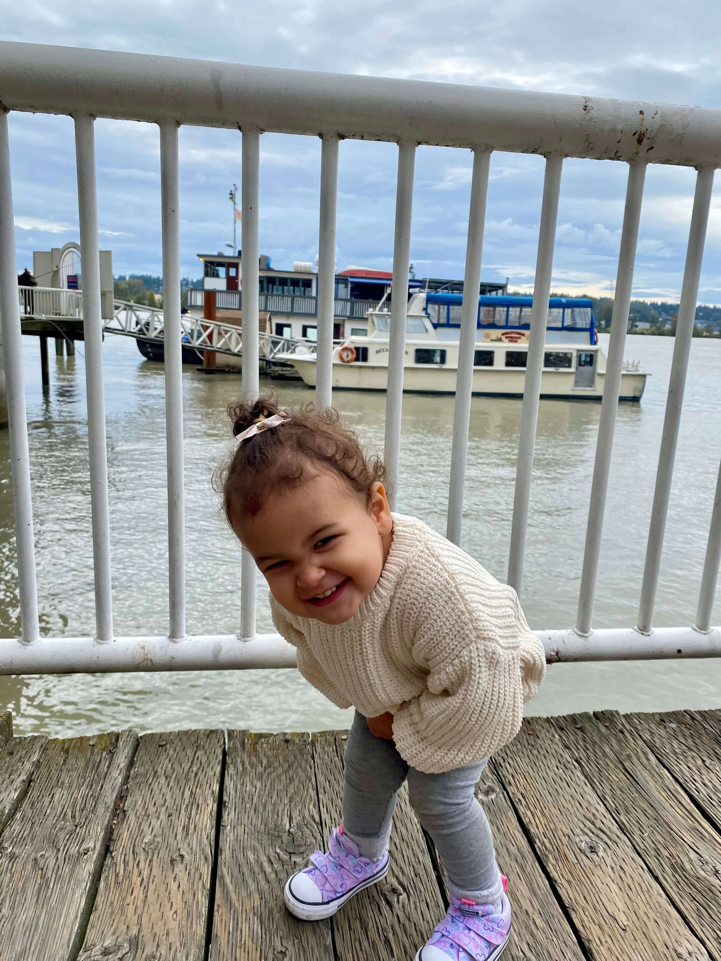 Little girl crouching and smiling on the New Westminser boardwalk.