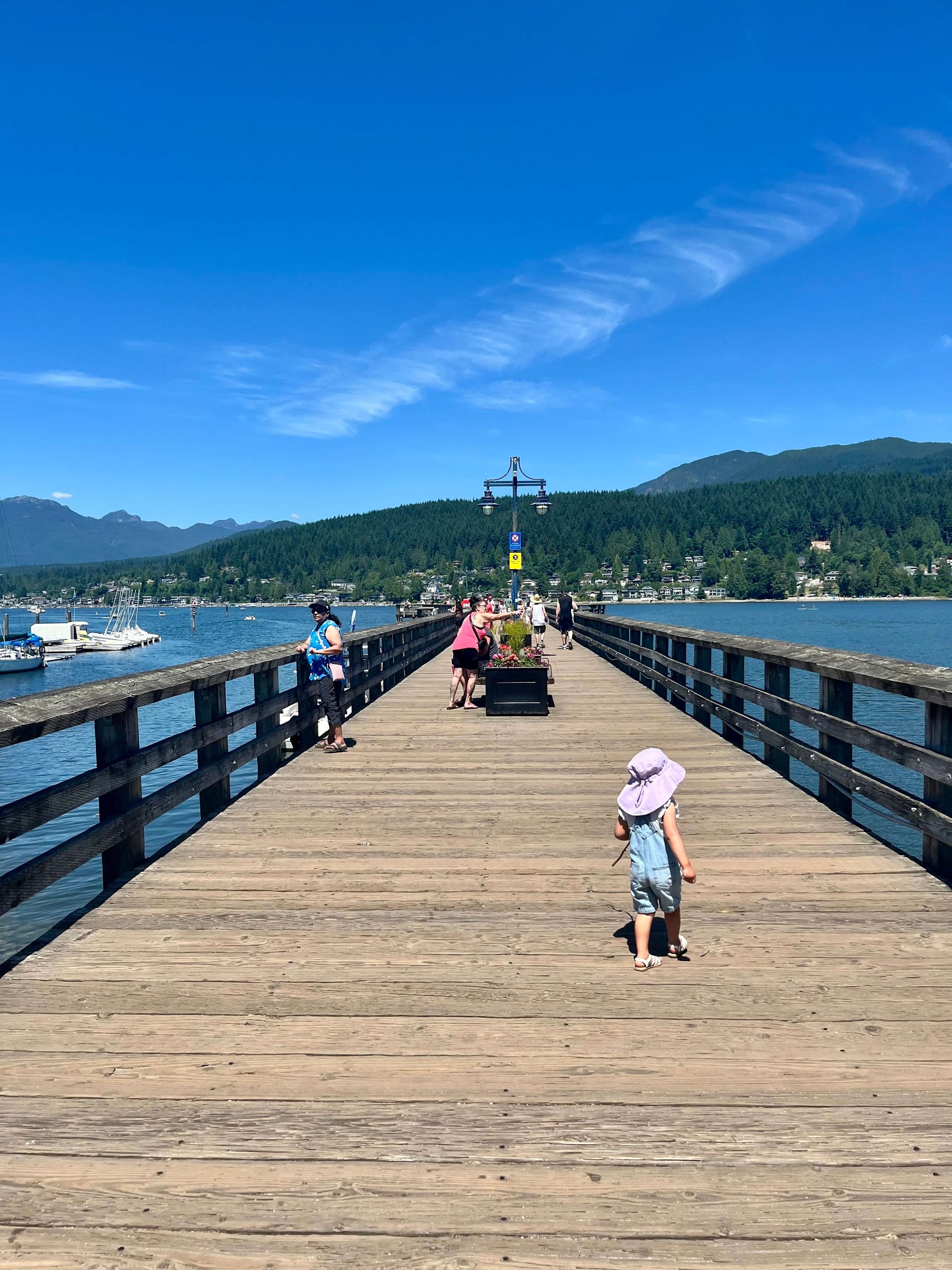 Little girl walking on a boardwalk. Blue sky and boars around