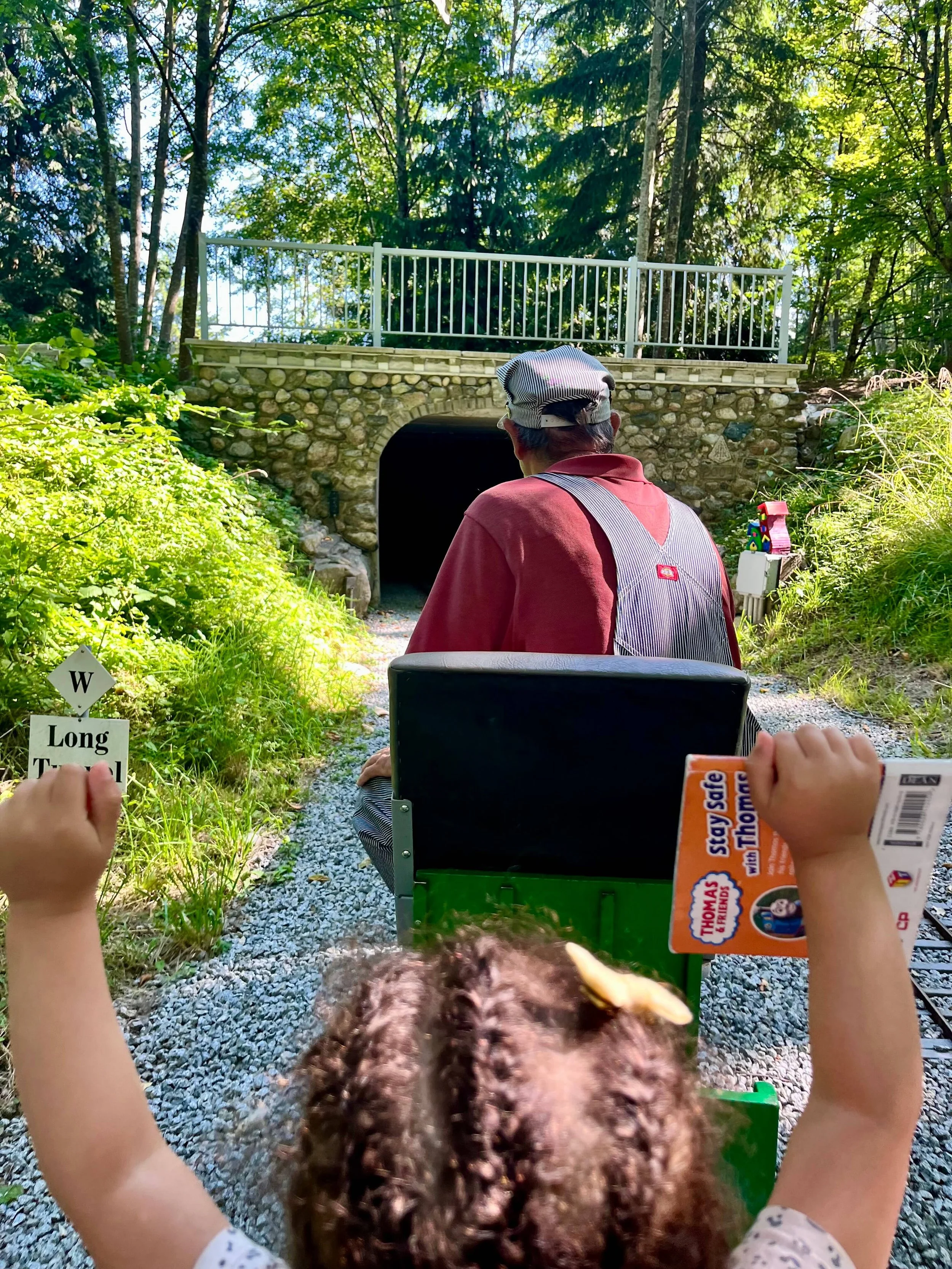 Little girl on a train holding up her hands as they approach a tunnel at Burnaby Central Railway