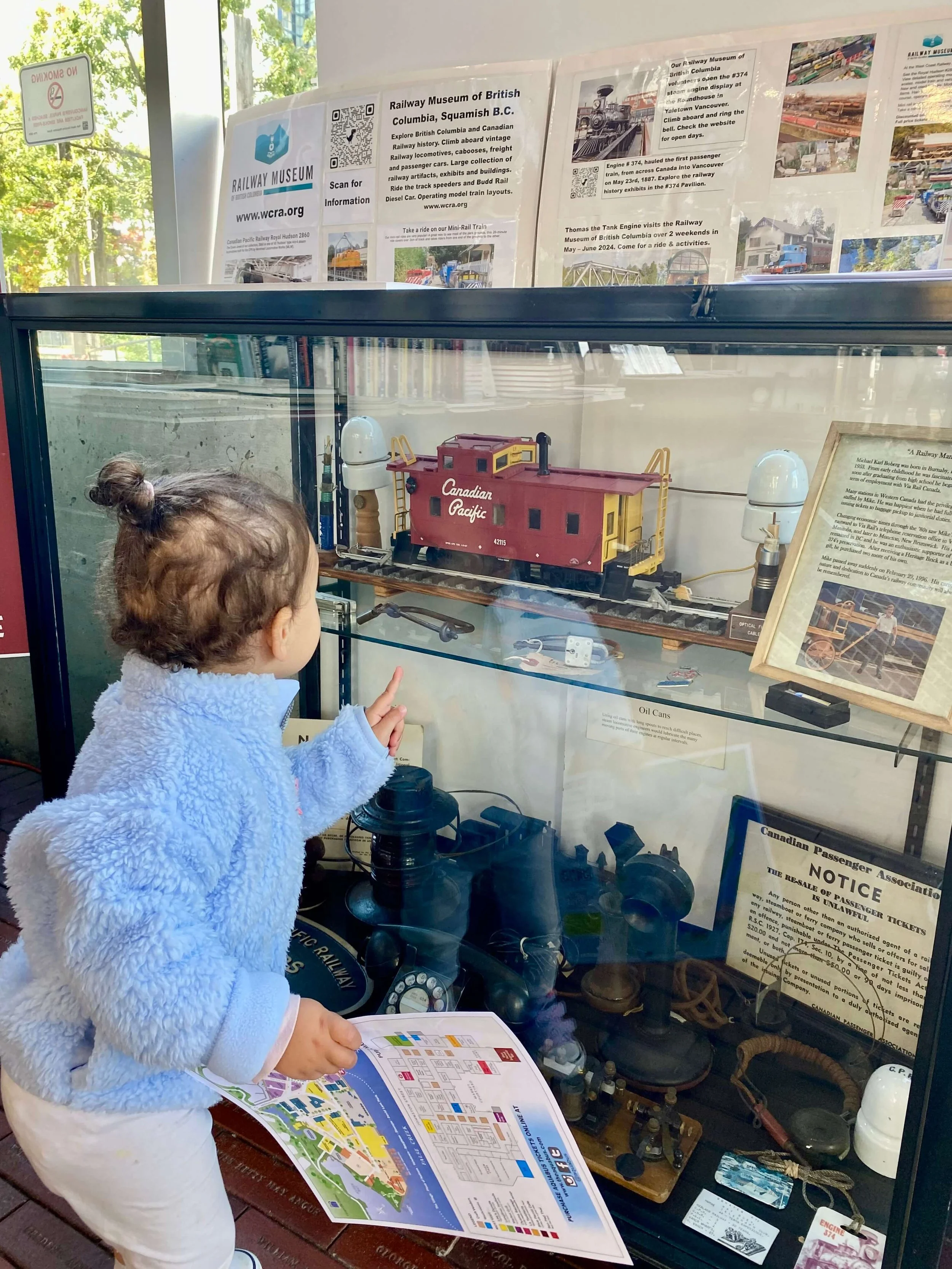 Little girl in blue sweater staring at a glass display case of train artifacts