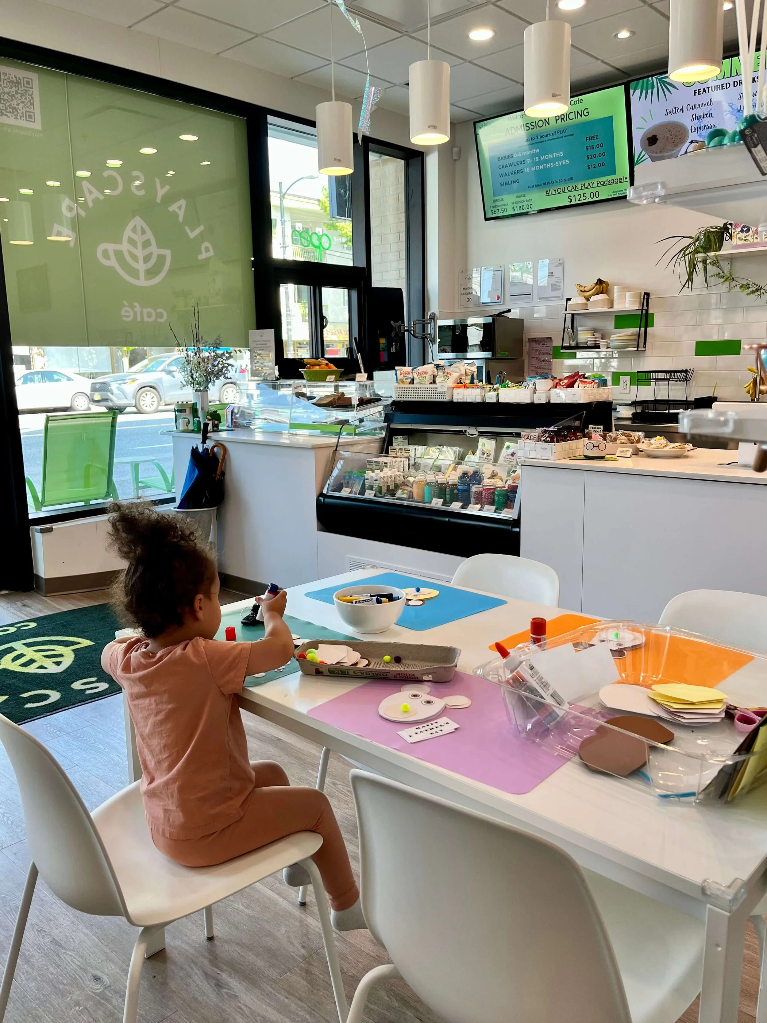Little girl dressed in peach clothing sitting at a table in a cafe and making a craft