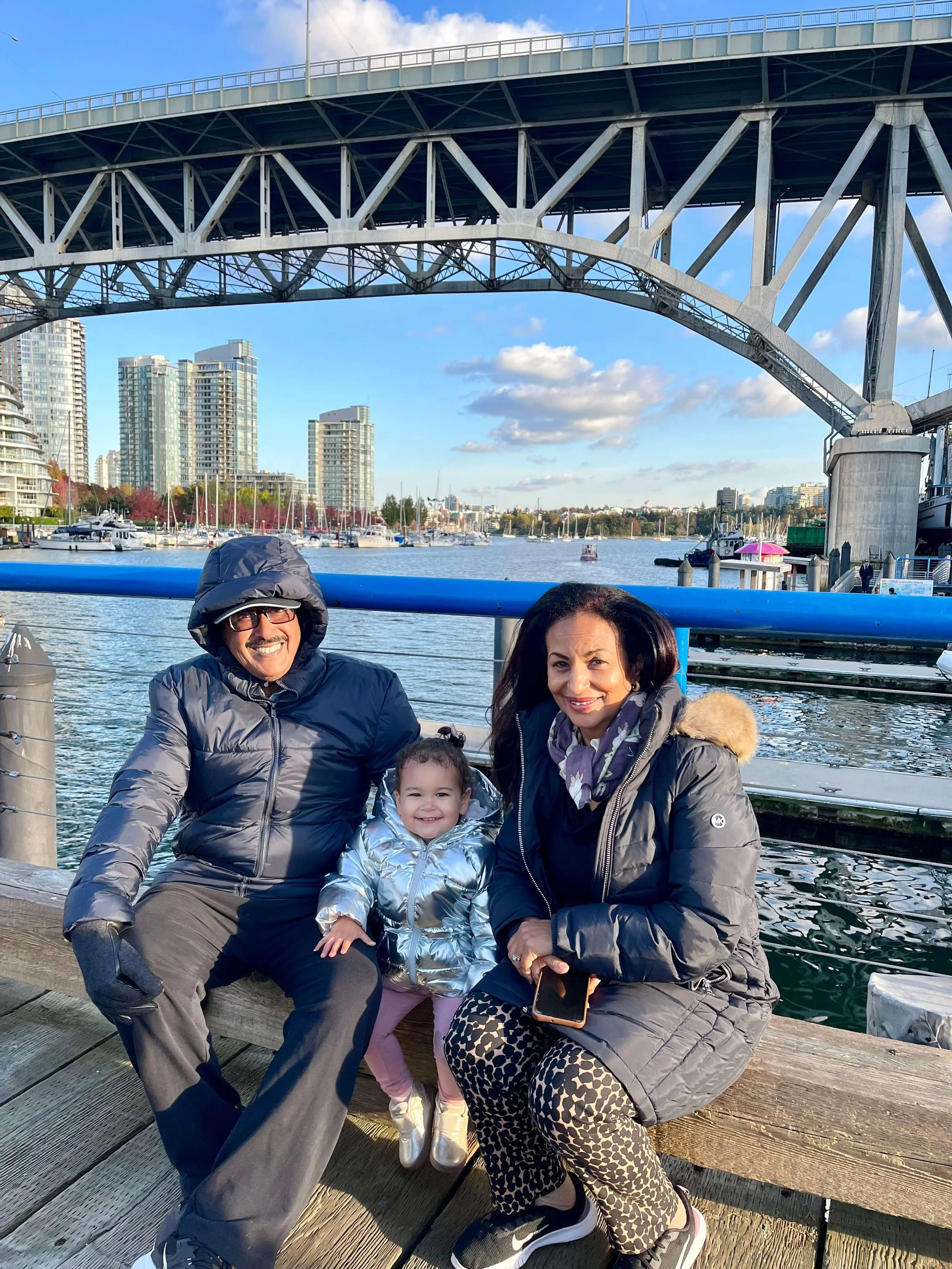 Little girl sitting between her grand parents next to the Granville Island waterfront.