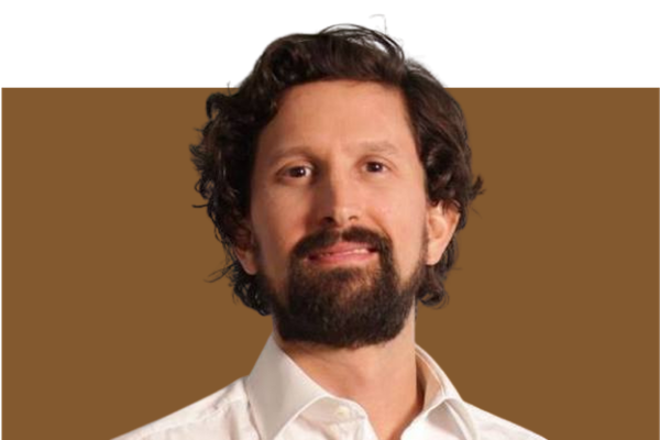 Portrait of a man with dark curly hair and a beard, wearing a white shirt, against a brown background.
