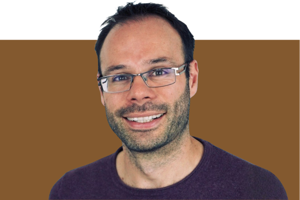 Portrait of a smiling man wearing glasses and a dark purple shirt, with a multicolored background.