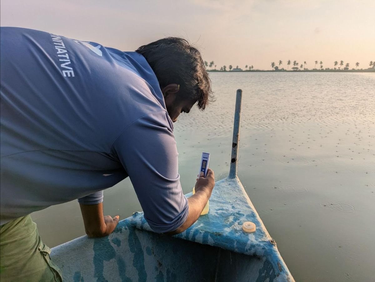A man leaning over a boat on a body of water, with palm trees in the background during sunset.